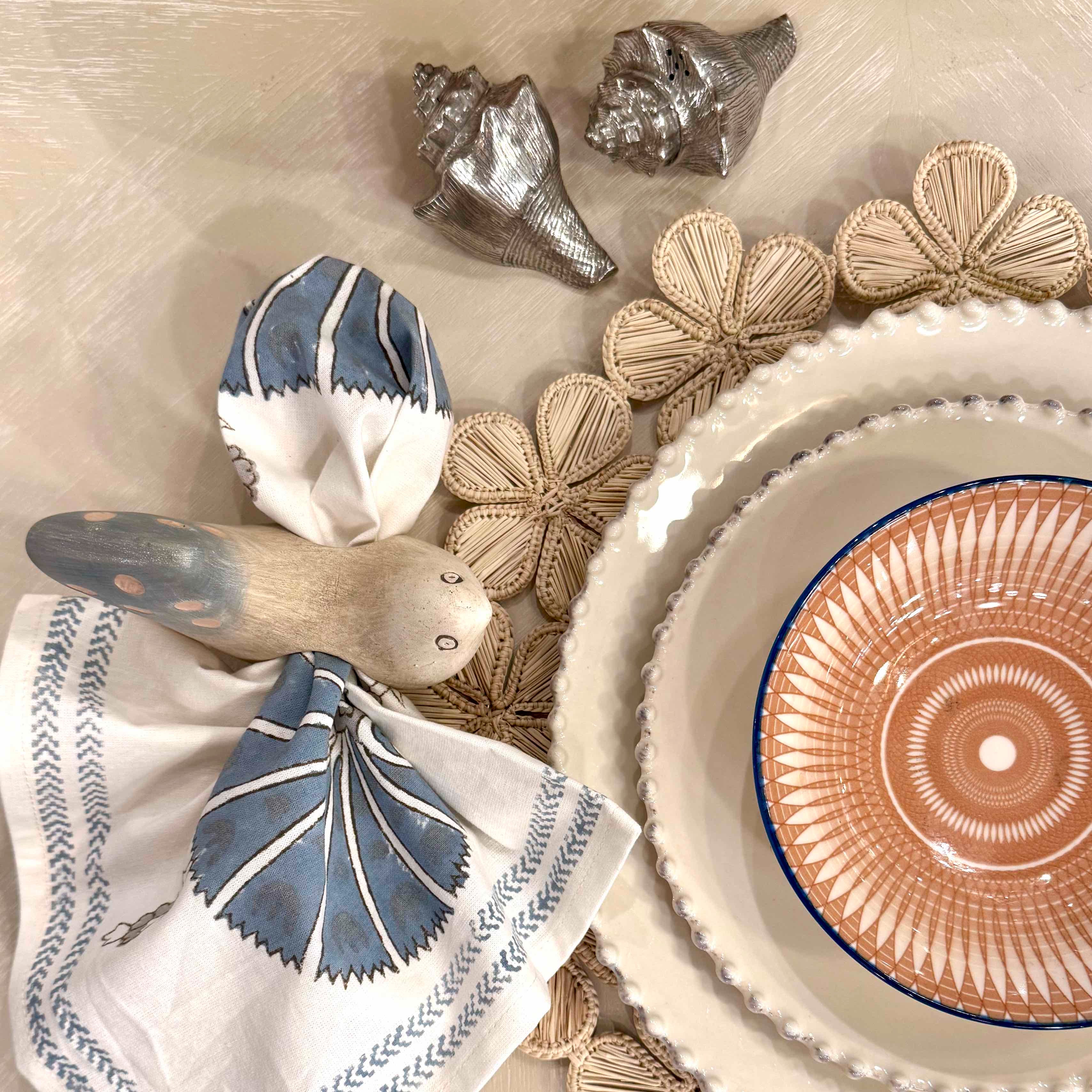 Decorative setting with ceramic plates, shell-shaped objects, and patterned napkins on a textured surface.