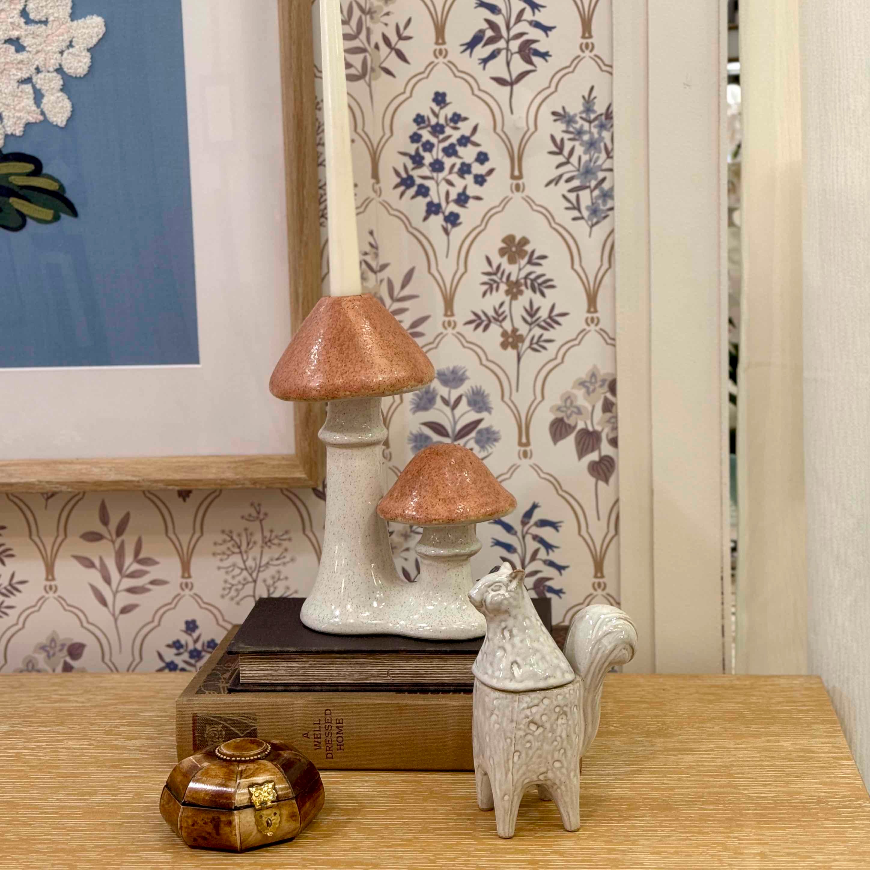 Decorative items including a mushroom-shaped lamp and a cat-shaped box on a wooden surface with a patterned wallpaper background.
