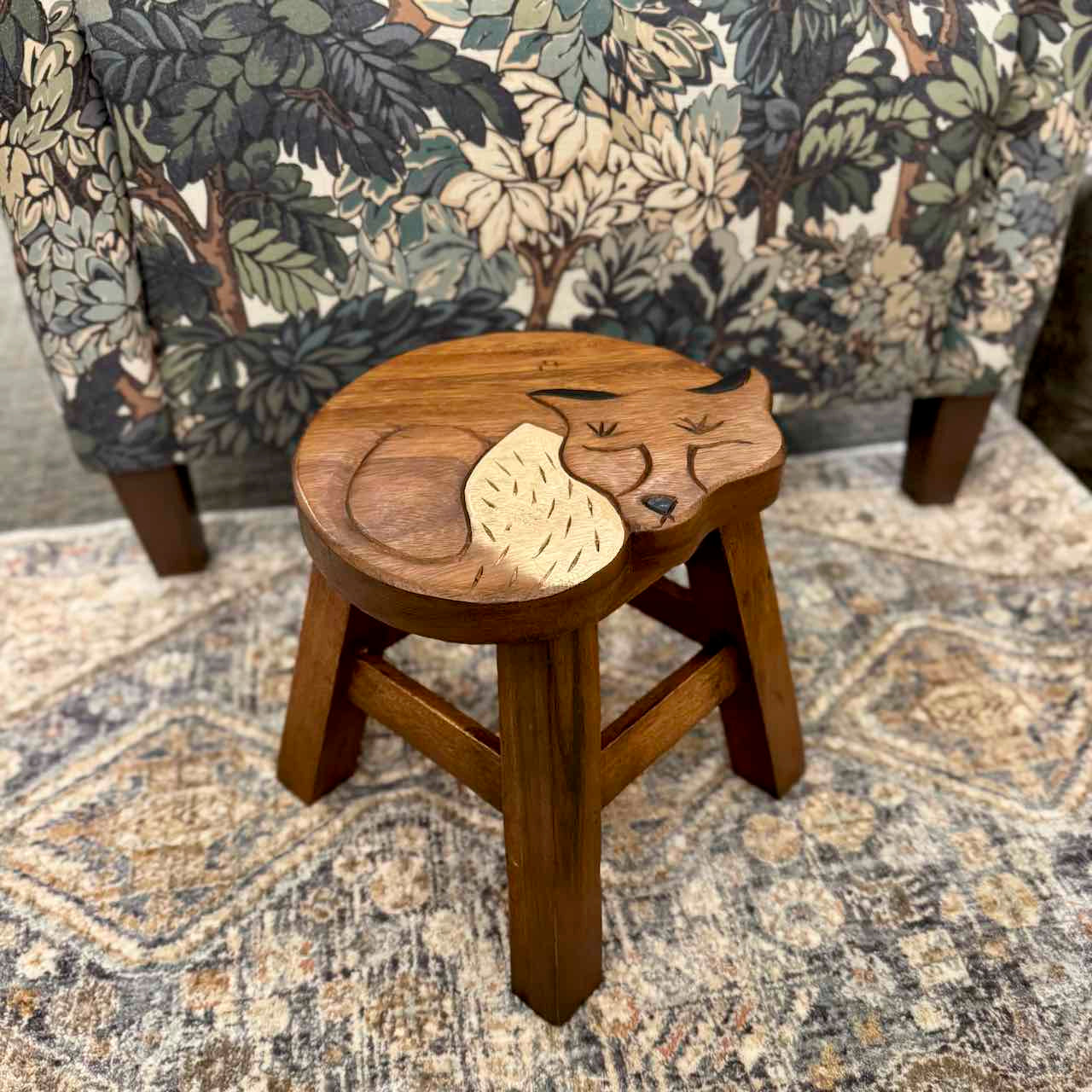 Wooden stool with a leaf design on a patterned rug