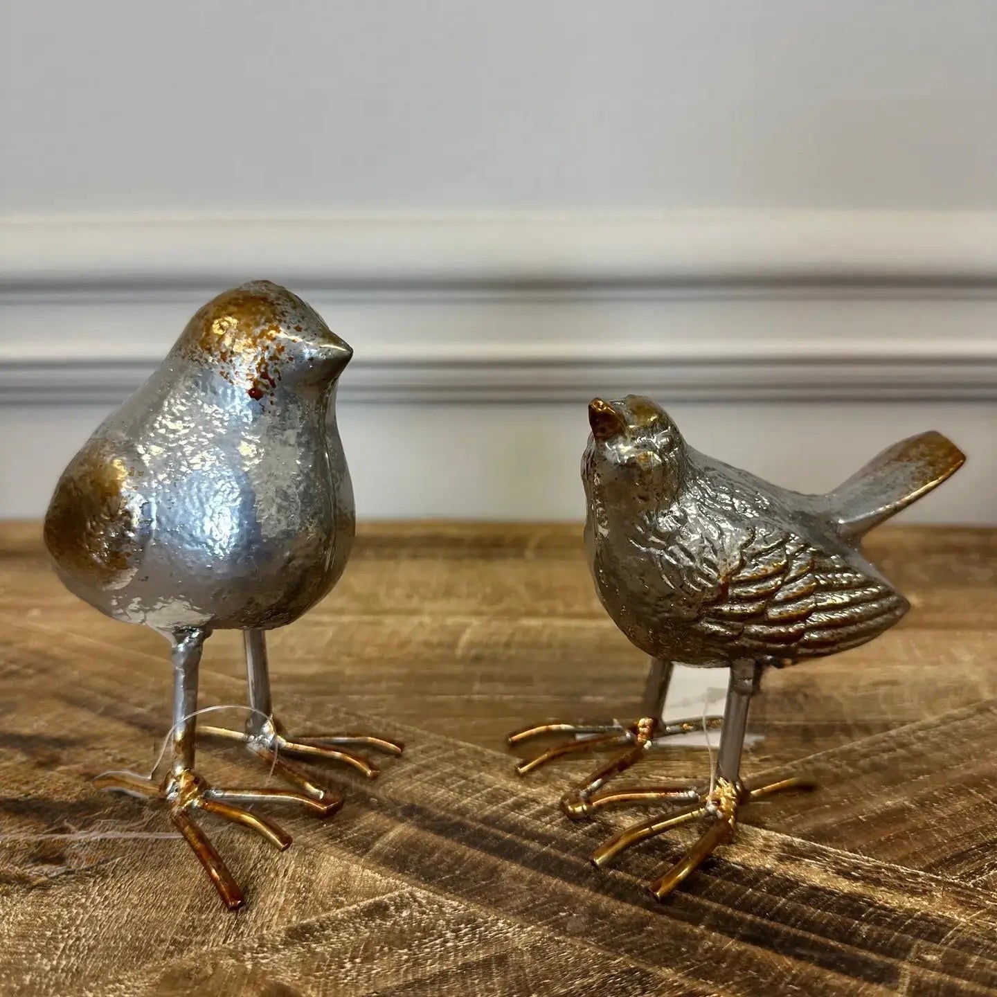 Two metallic bird figurines on a wooden surface with a neutral background