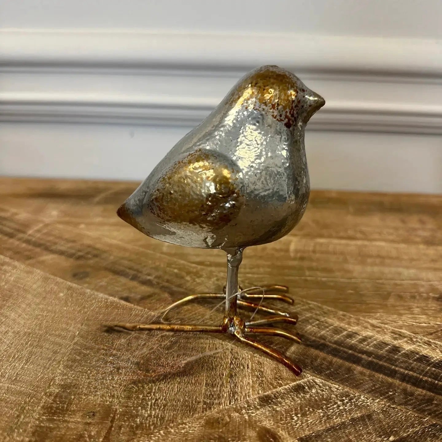 Decorative bird figurine with gold and silver finish on a wooden surface