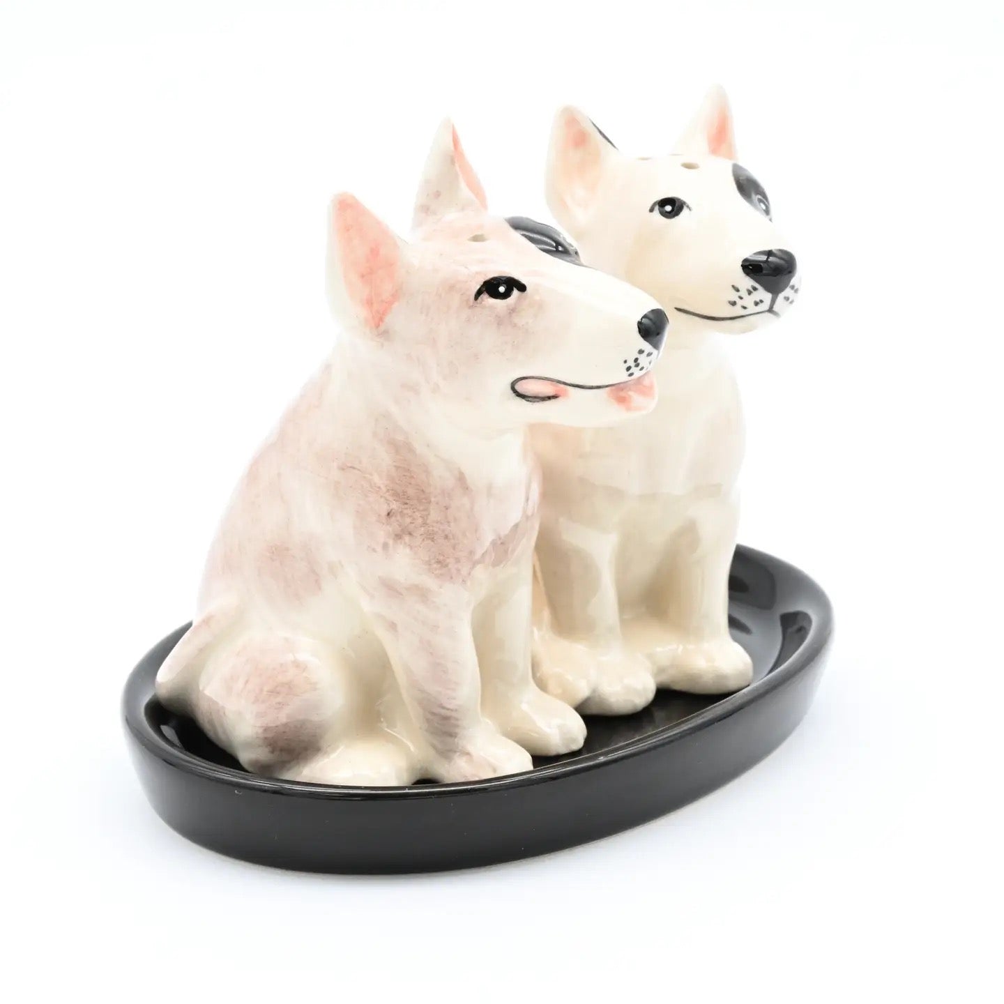 Two ceramic dog figurines sitting on a black round base against a white background