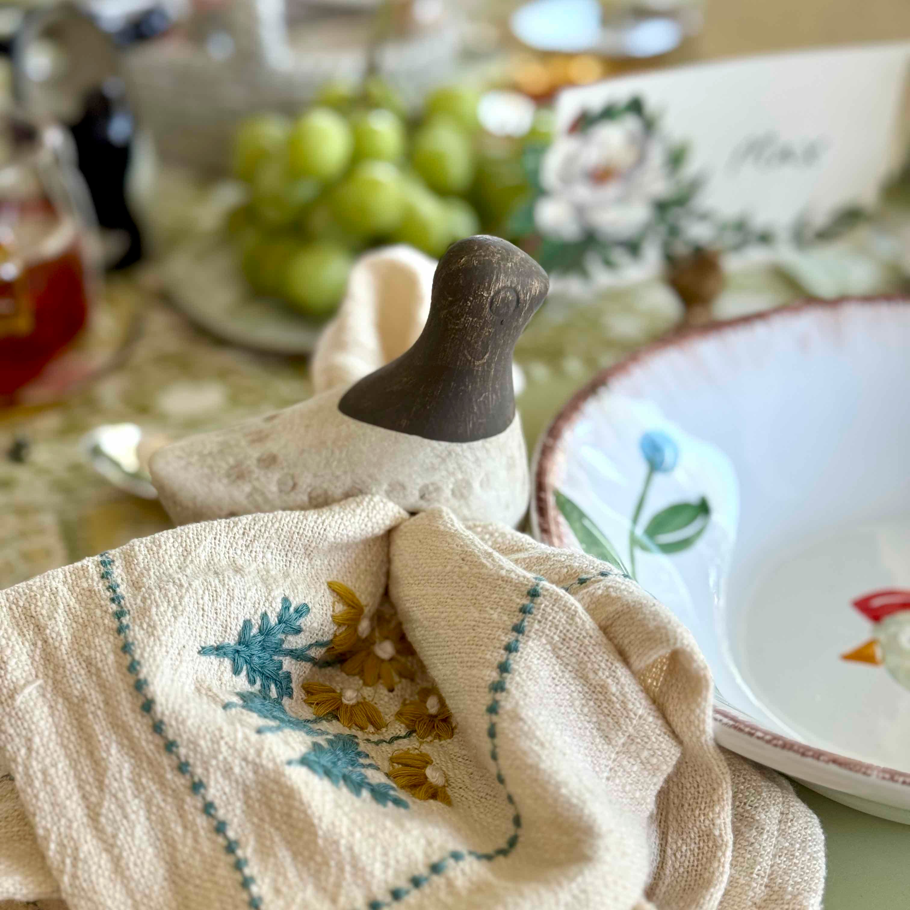 Decorative ceramic bird with a towel featuring floral embroidery on a table setting.