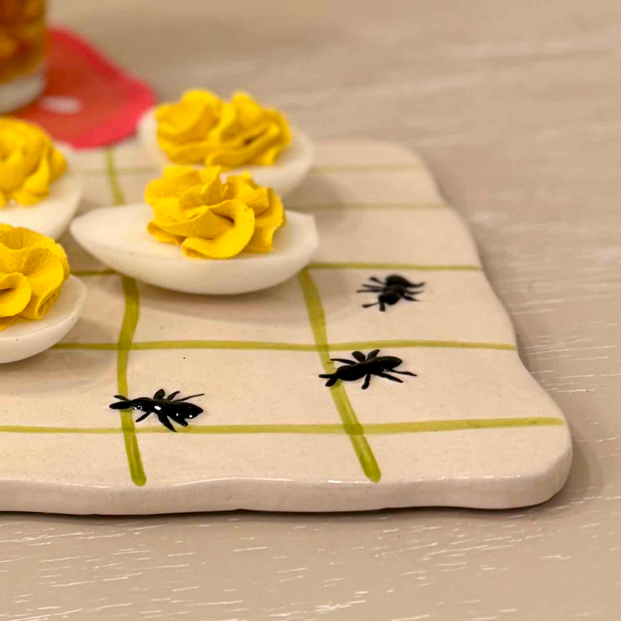 Deviled eggs with yellow garnishes on a checkered board with black ants.