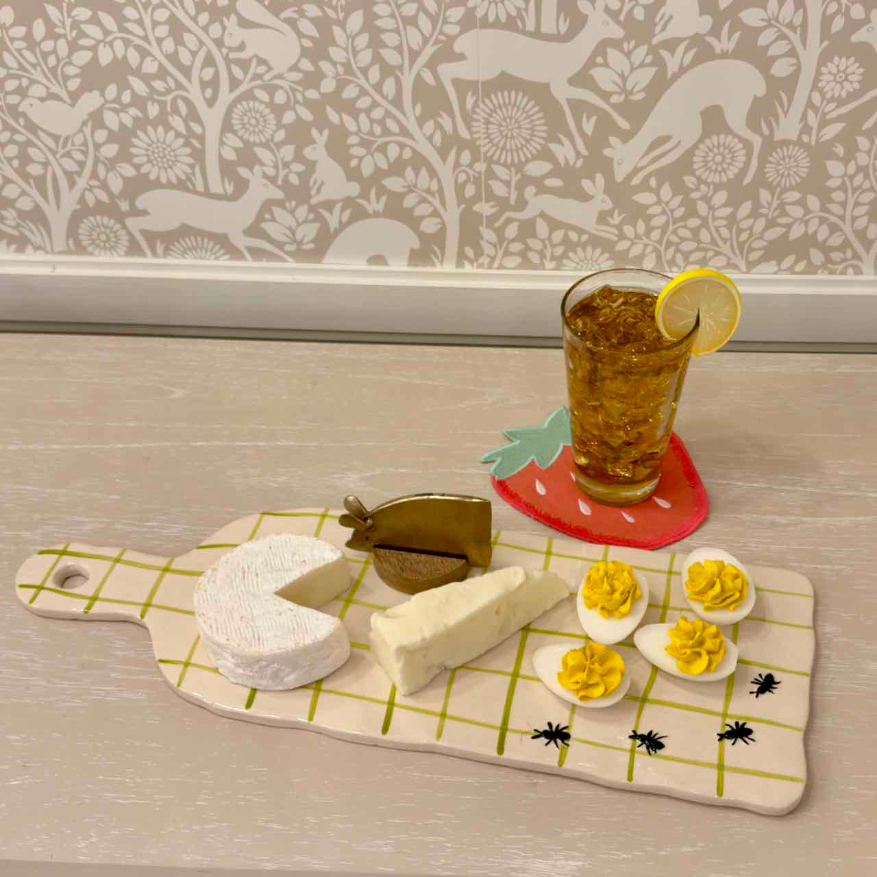 Butter, cheese, and deviled eggs on a checkered board with a glass of iced tea.