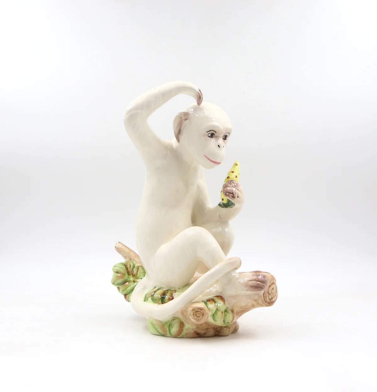 White ceramic monkey figurine holding a banana on a white background