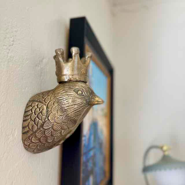 Decorative wall piece of a bird with a crown on a light-colored wall.