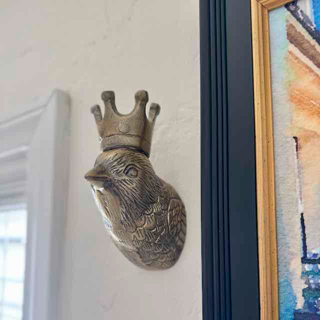 Decorative wall piece with a bird head and crown on a white wall.