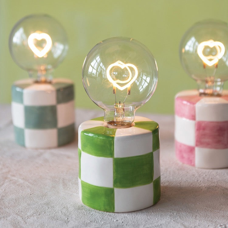 Three decorative lamps with checkered bases and heart-shaped light bulbs on a light surface.