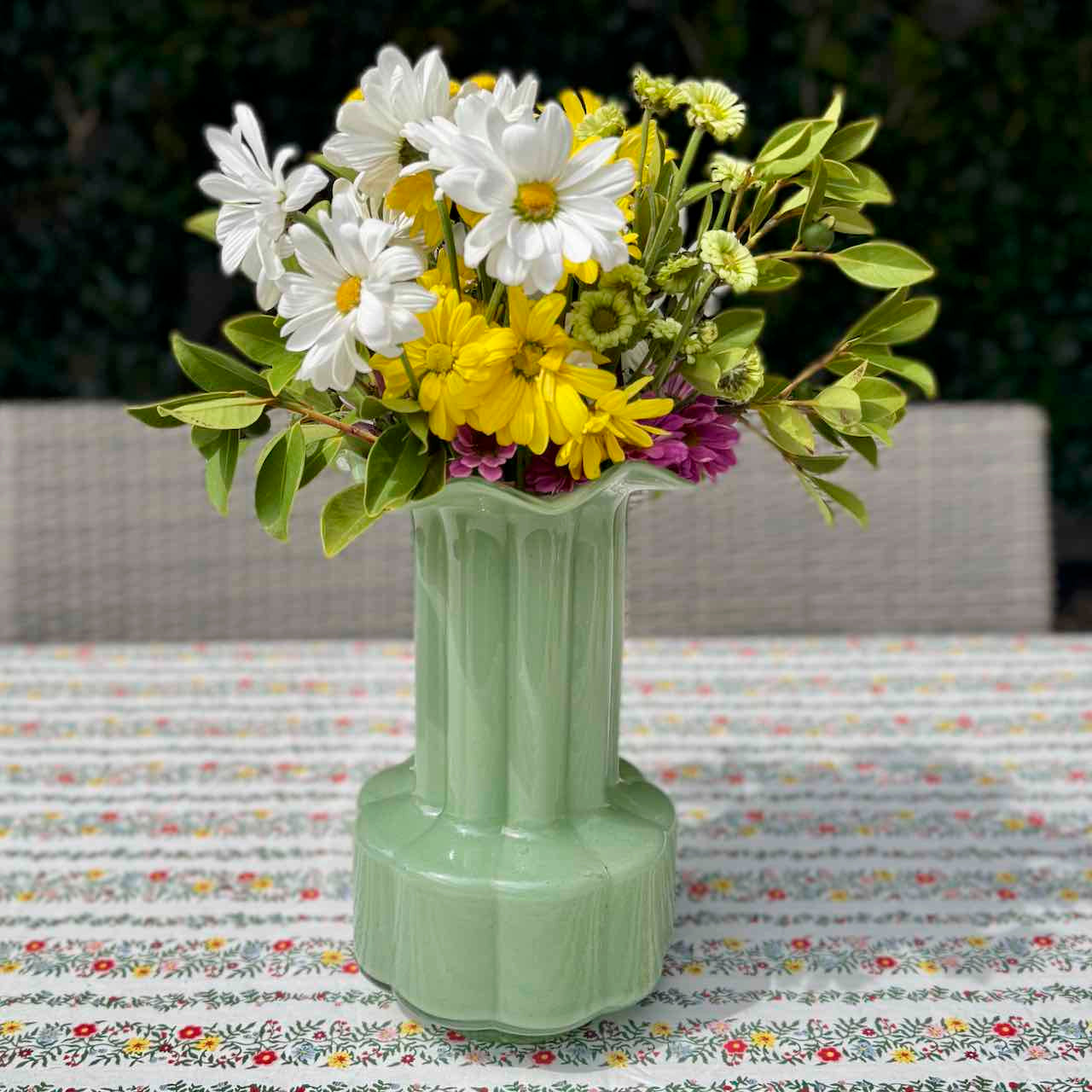 Green vase with flowers on a patterned tablecloth