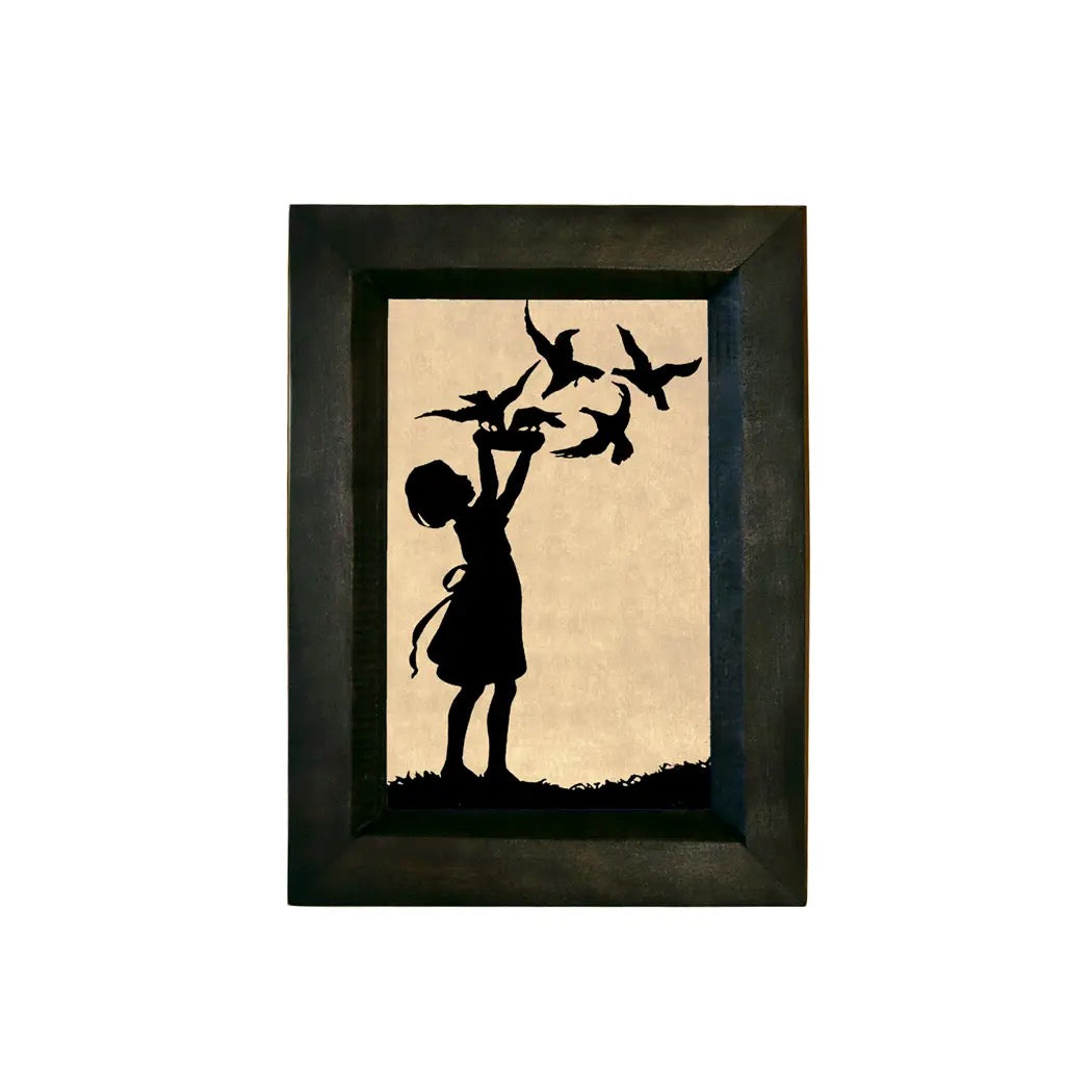 Framed silhouette artwork of a child releasing birds on beige paper.