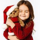 Child in a red dress holding a teddy bear wearing a Santa hat on a white background