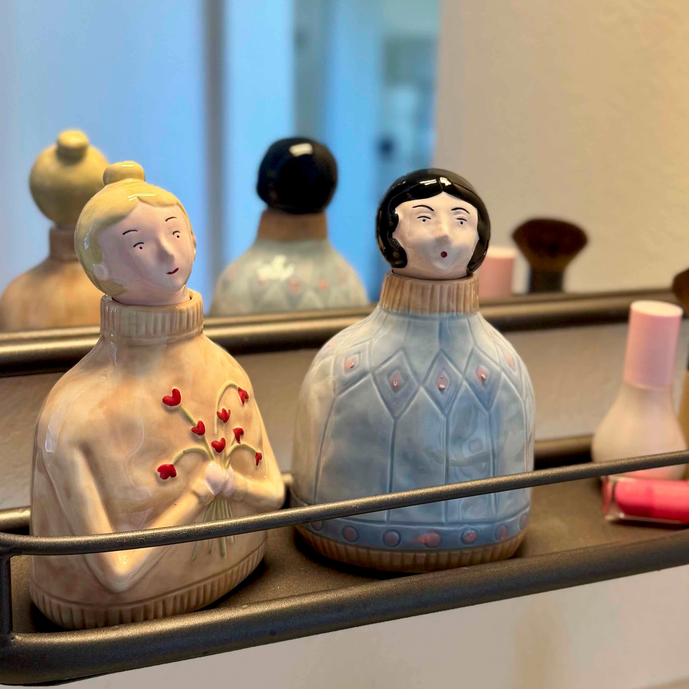 Three ceramic figurines with different hairstyles and outfits on a shelf.
