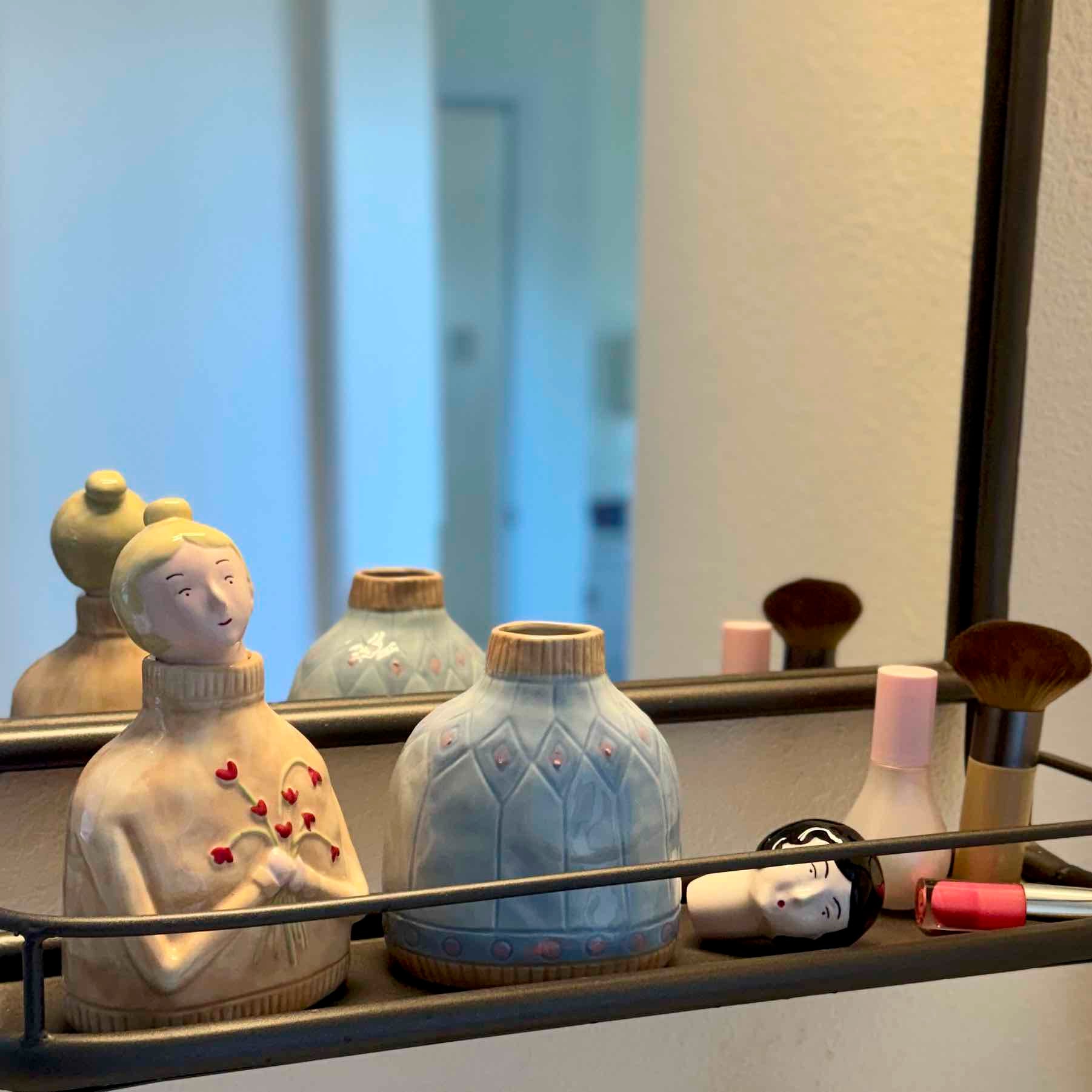 Decorative items including a figurine, vases, and makeup brushes on a surface with a mirror in the background.