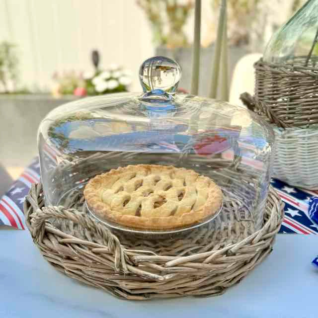 Pie under a glass cloche on a woven basket with a blurred outdoor background