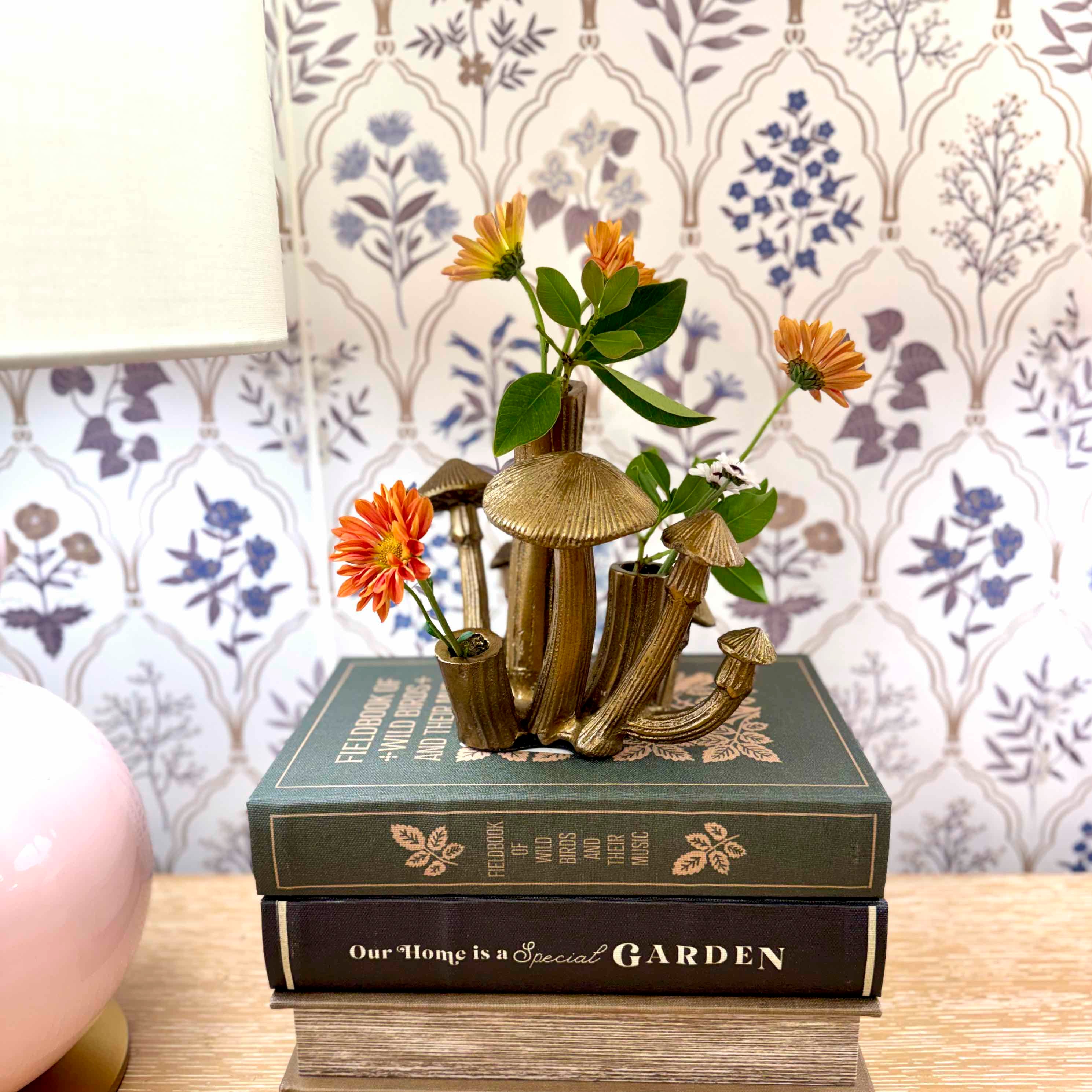 Decorative arrangement of mushrooms and flowers on a book with a floral-patterned wallpaper background.