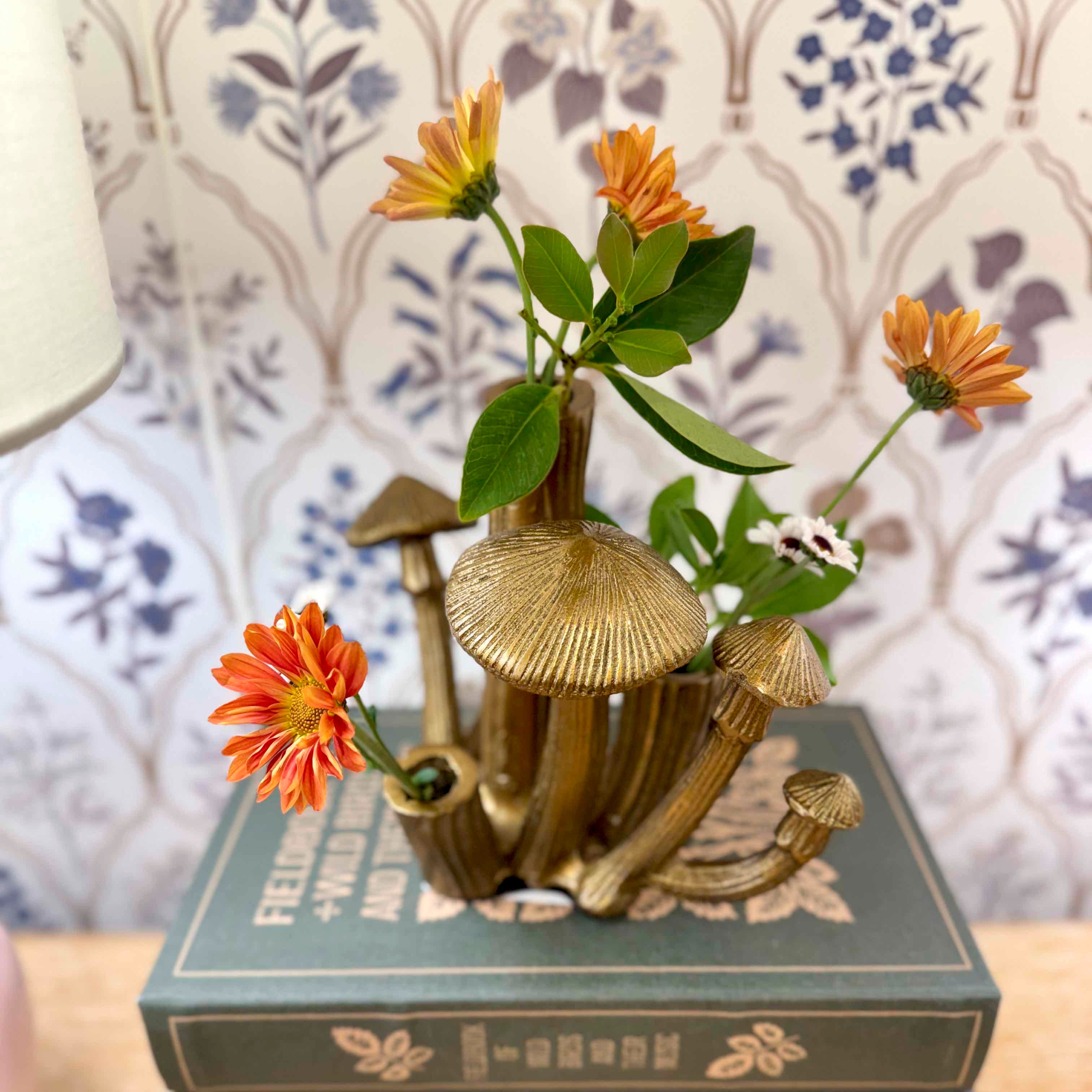 Decorative mushroom sculpture with flowers on a book against a patterned wall.