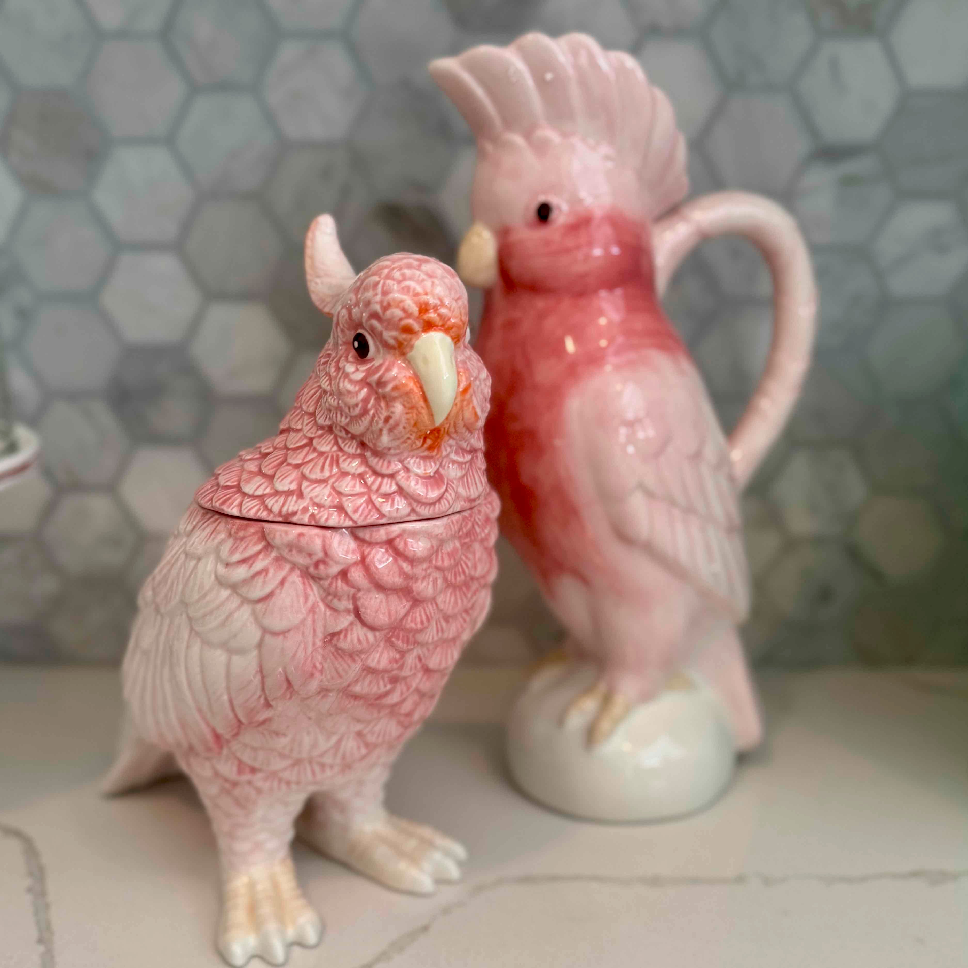 Two ceramic parrot figurines on a tiled surface with a hexagonal tile pattern.