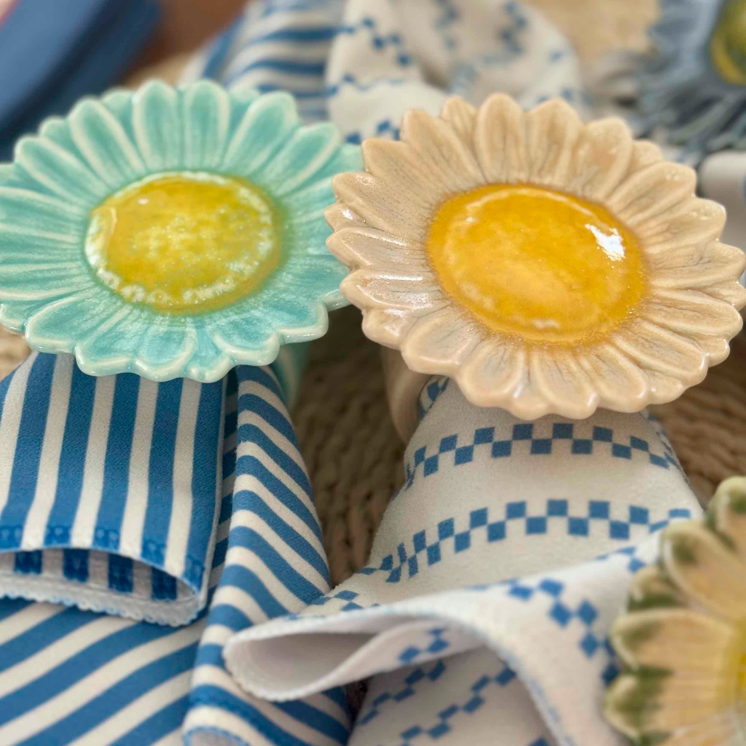 Two ceramic flower-shaped containers with green and yellow centers on a blue and white striped fabric background.