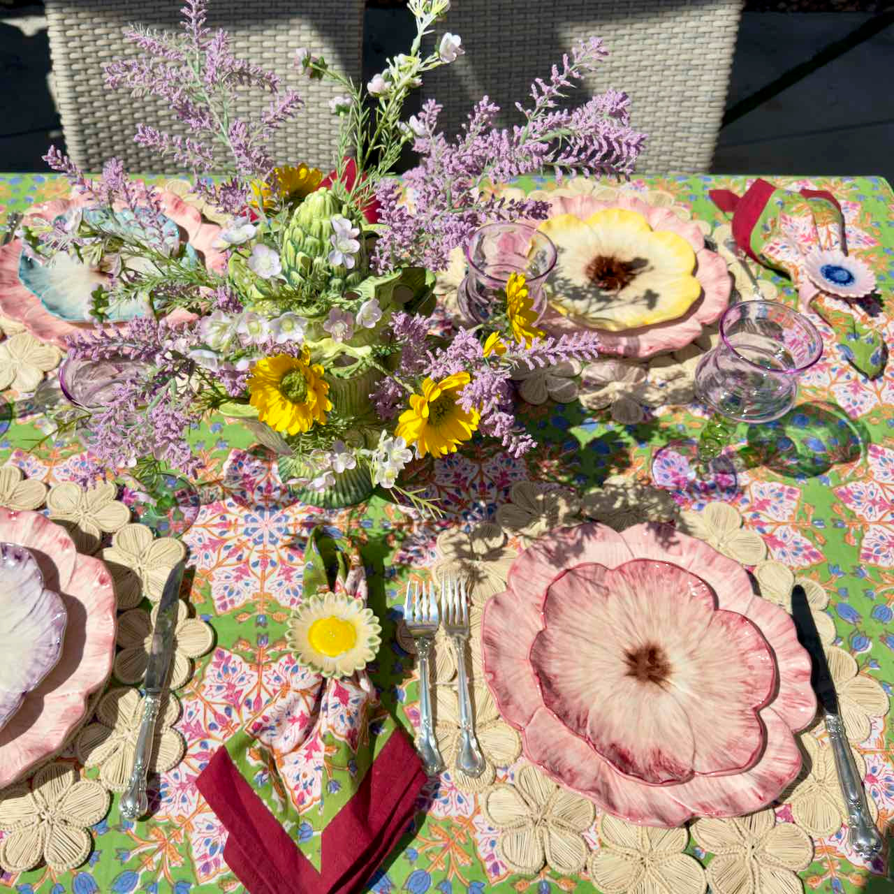 Decorative table setting with floral plates, napkins, and cutlery on a colorful tablecloth.