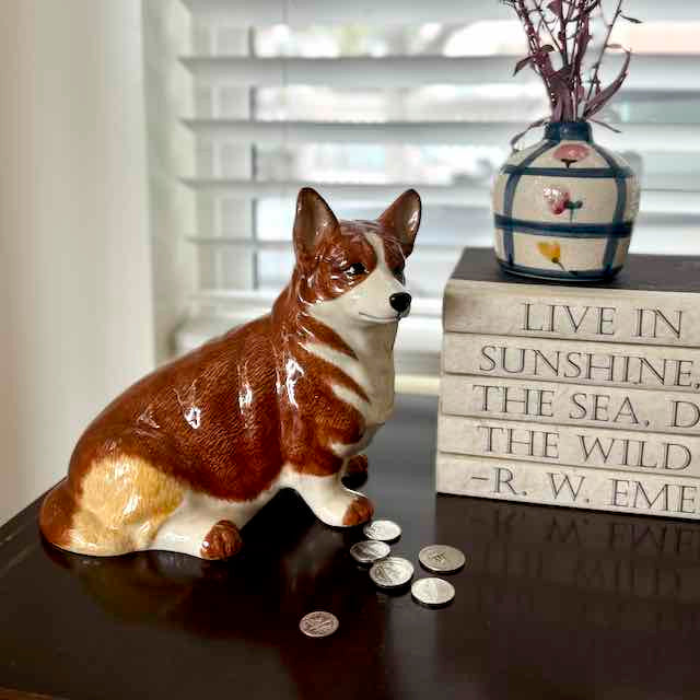 Corgi dog figurine with coins on a surface next to a vase and motivational quote block.
