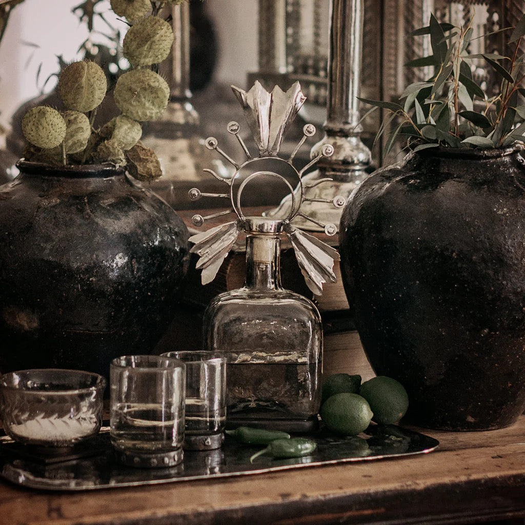 Decorative still life with bottles, glasses, and plants on a wooden surface.