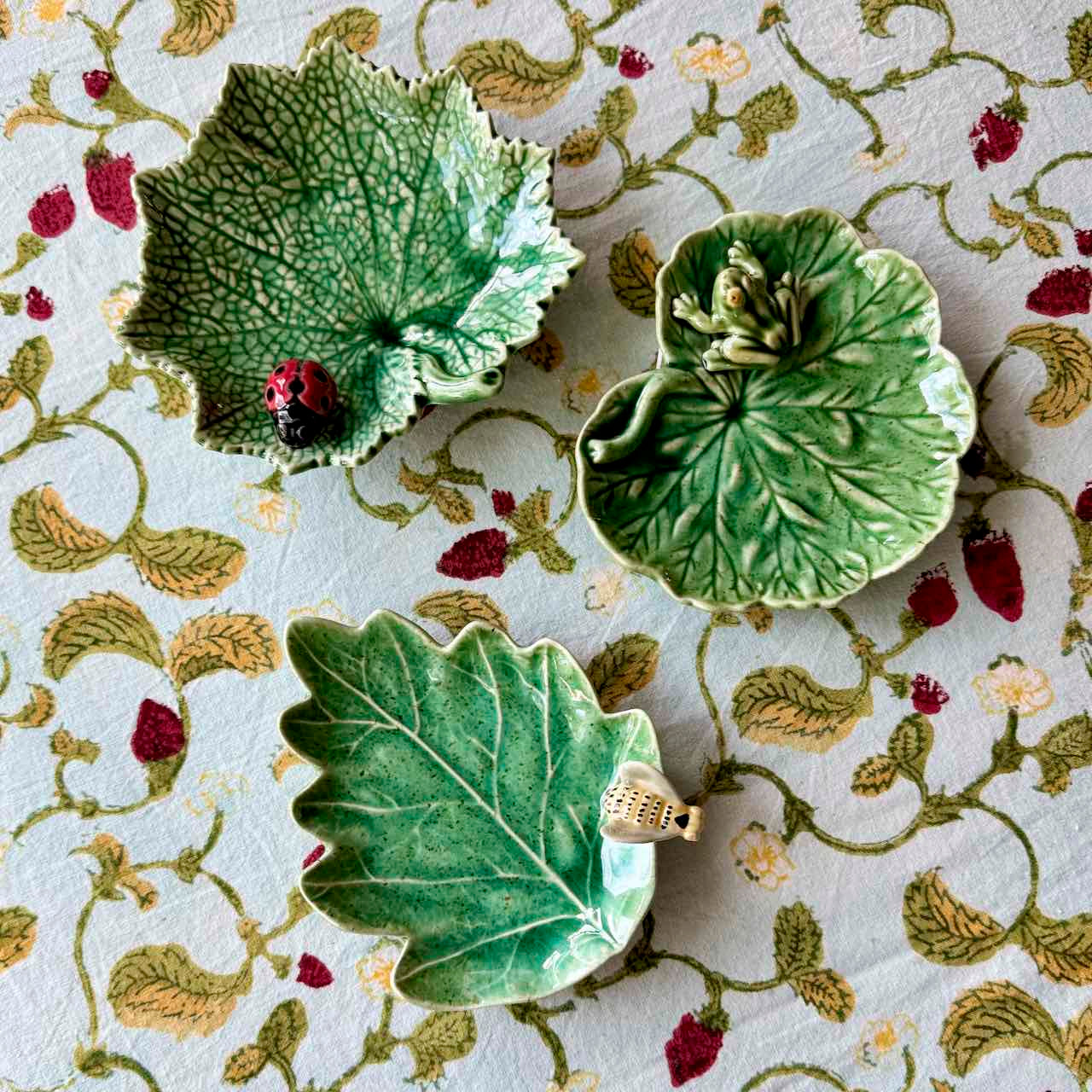 Three green ceramic leaf-shaped dishes on a decorative fabric background