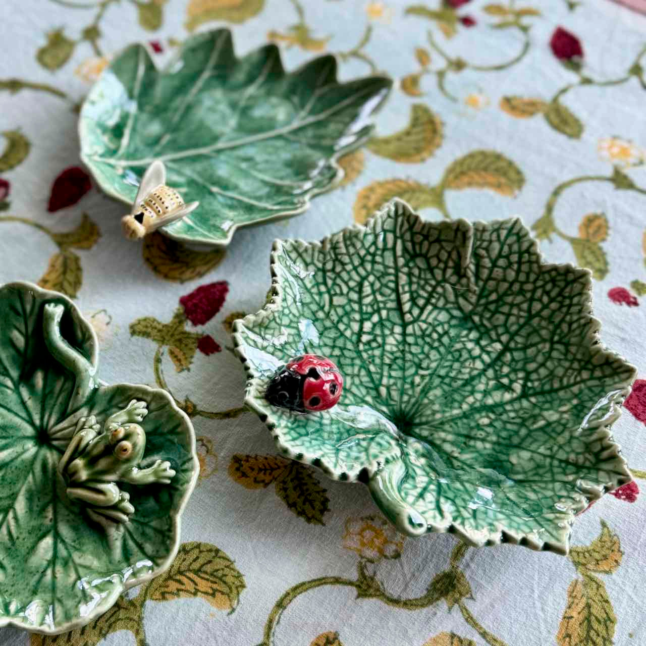 Three green ceramic leaf-shaped dishes on a floral tablecloth.