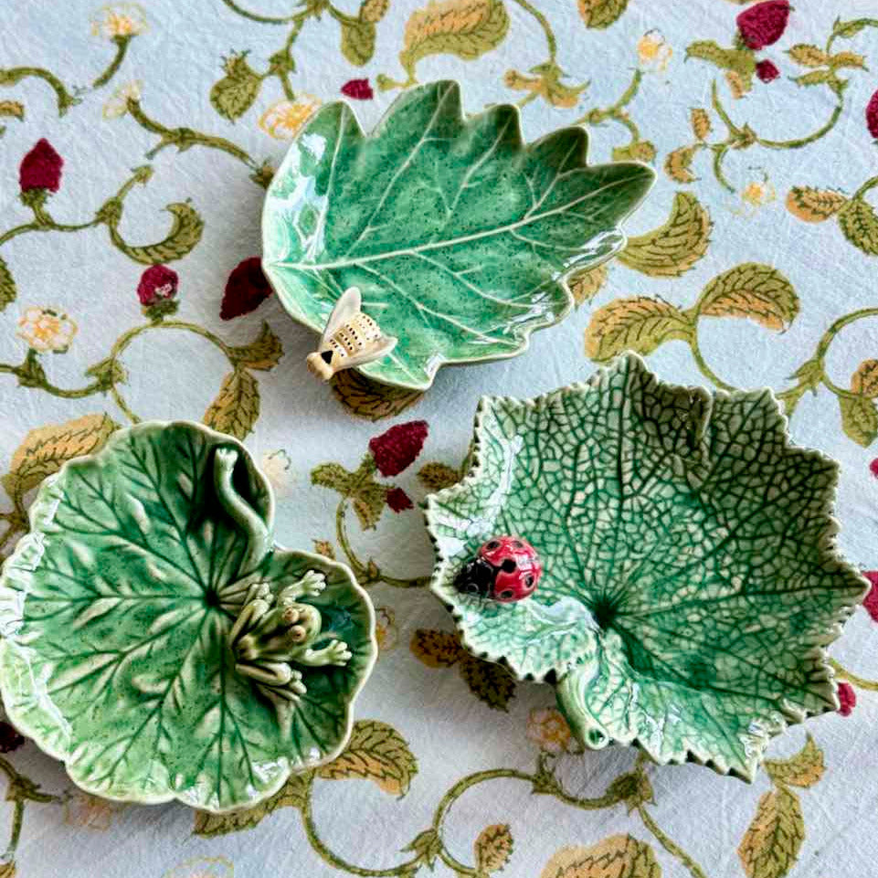 Three green leaf-shaped ceramic dishes on a floral-patterned fabric background