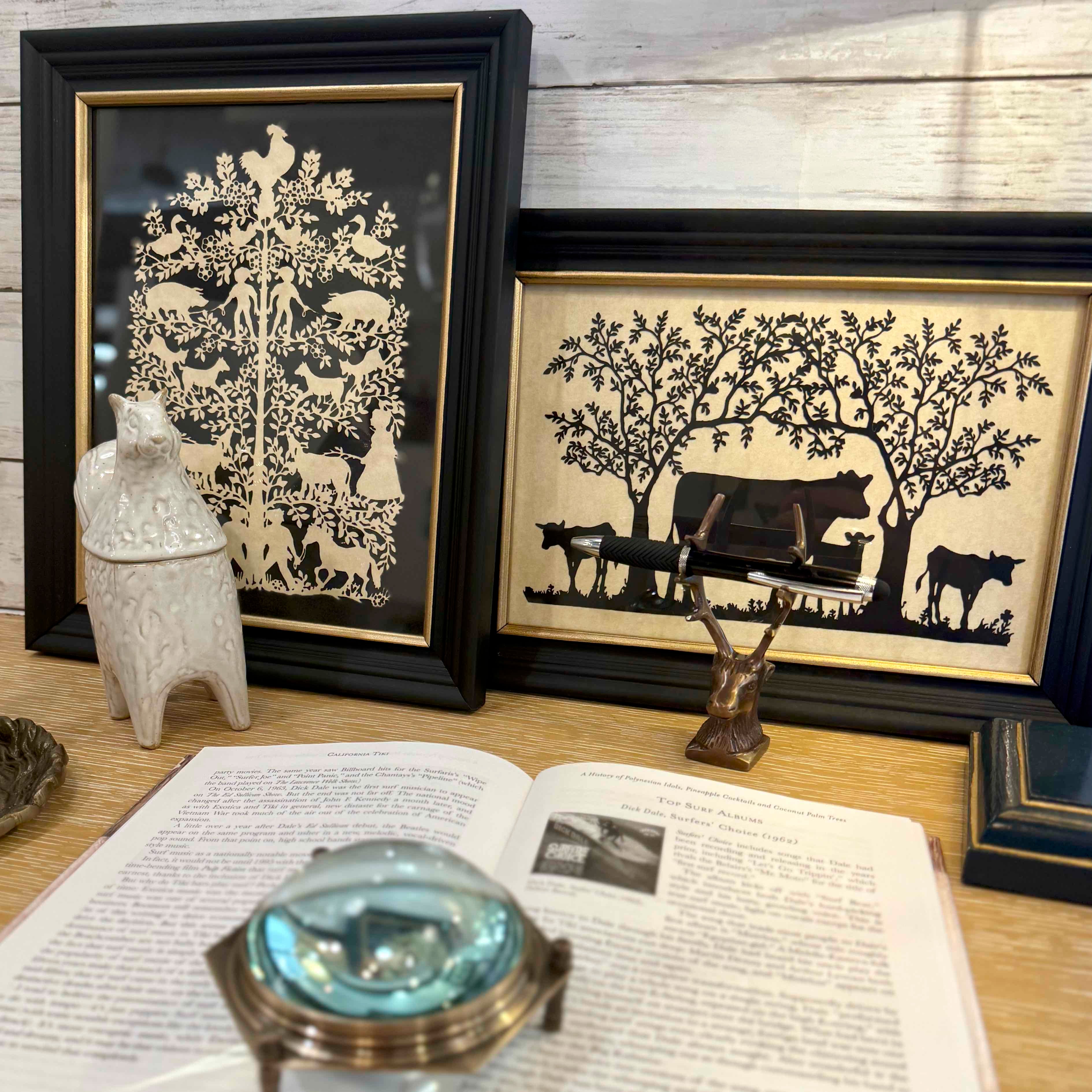 Two framed black and white silhouettes on a wooden surface with an open book and magnifying glass.