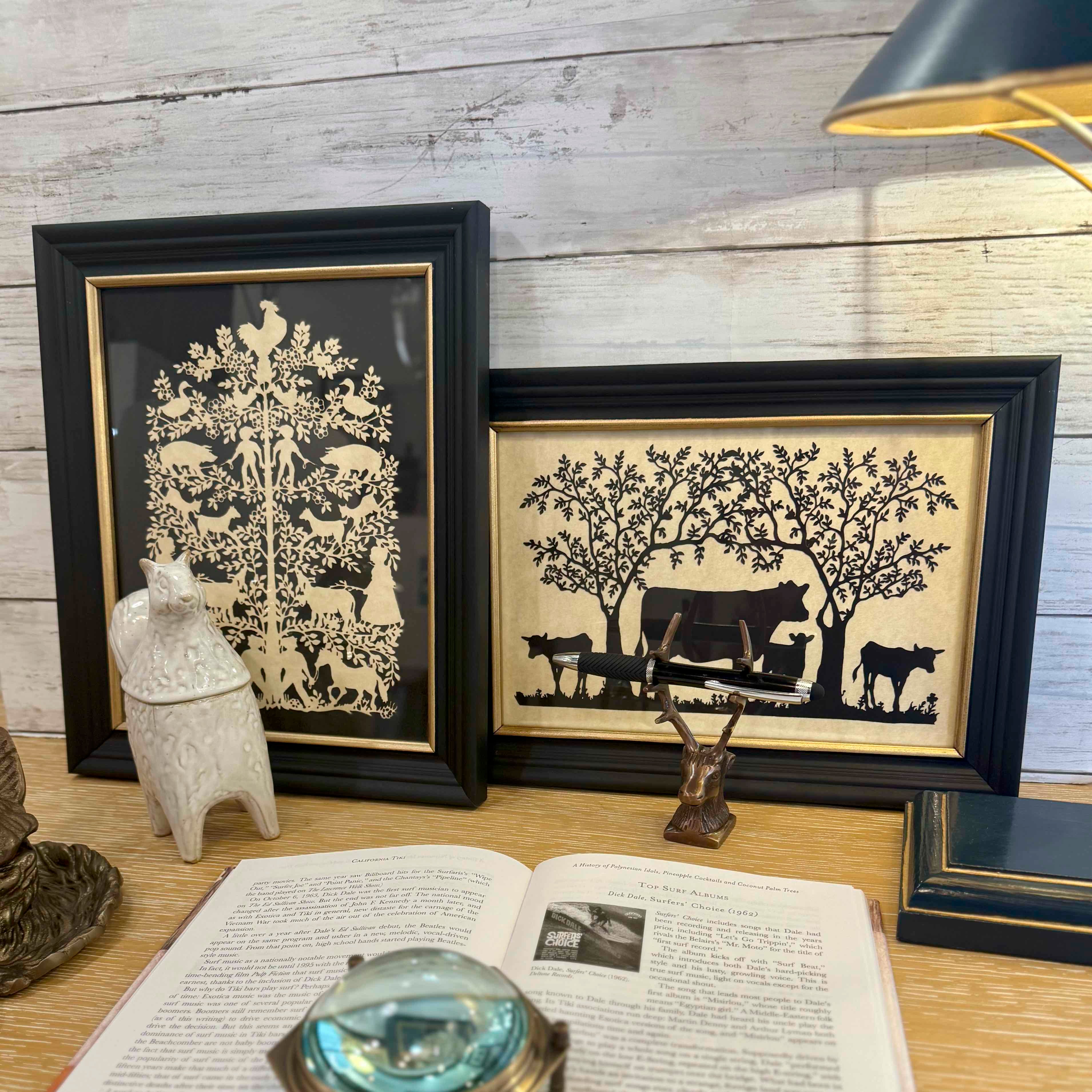 Two framed black and white silhouettes on a wooden surface with books and decorative items.
