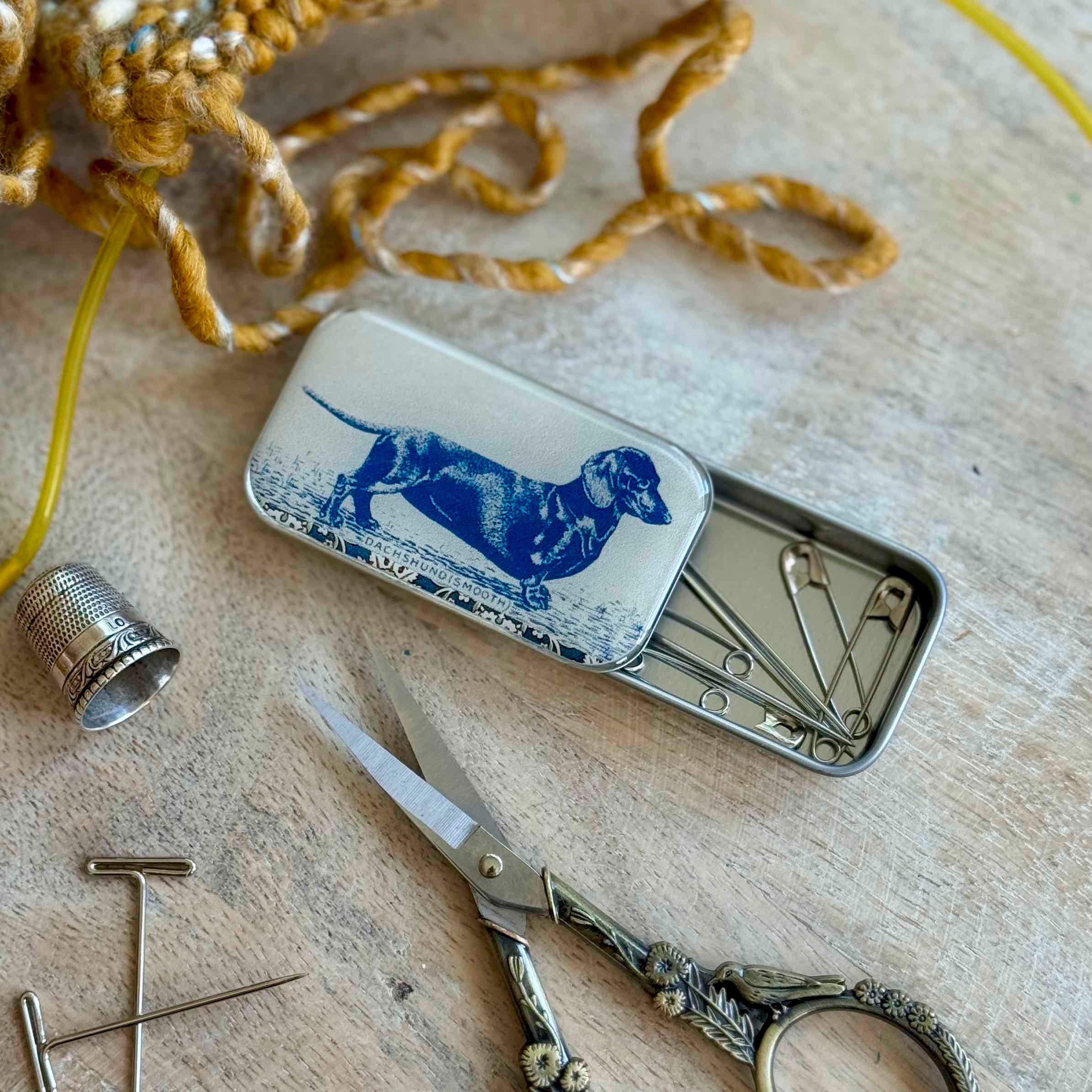 Small metal tin with sewing tools on a wooden surface