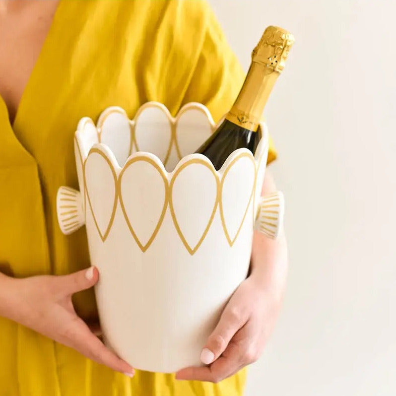 Person holding a decorative wine cooler with a bottle of champagne inside, wearing a yellow dress.
