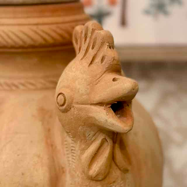 Terracotta sculpture of a rooster with a blurred background