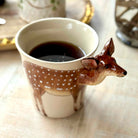 Ceramic mug with deer design filled with coffee on a light surface.