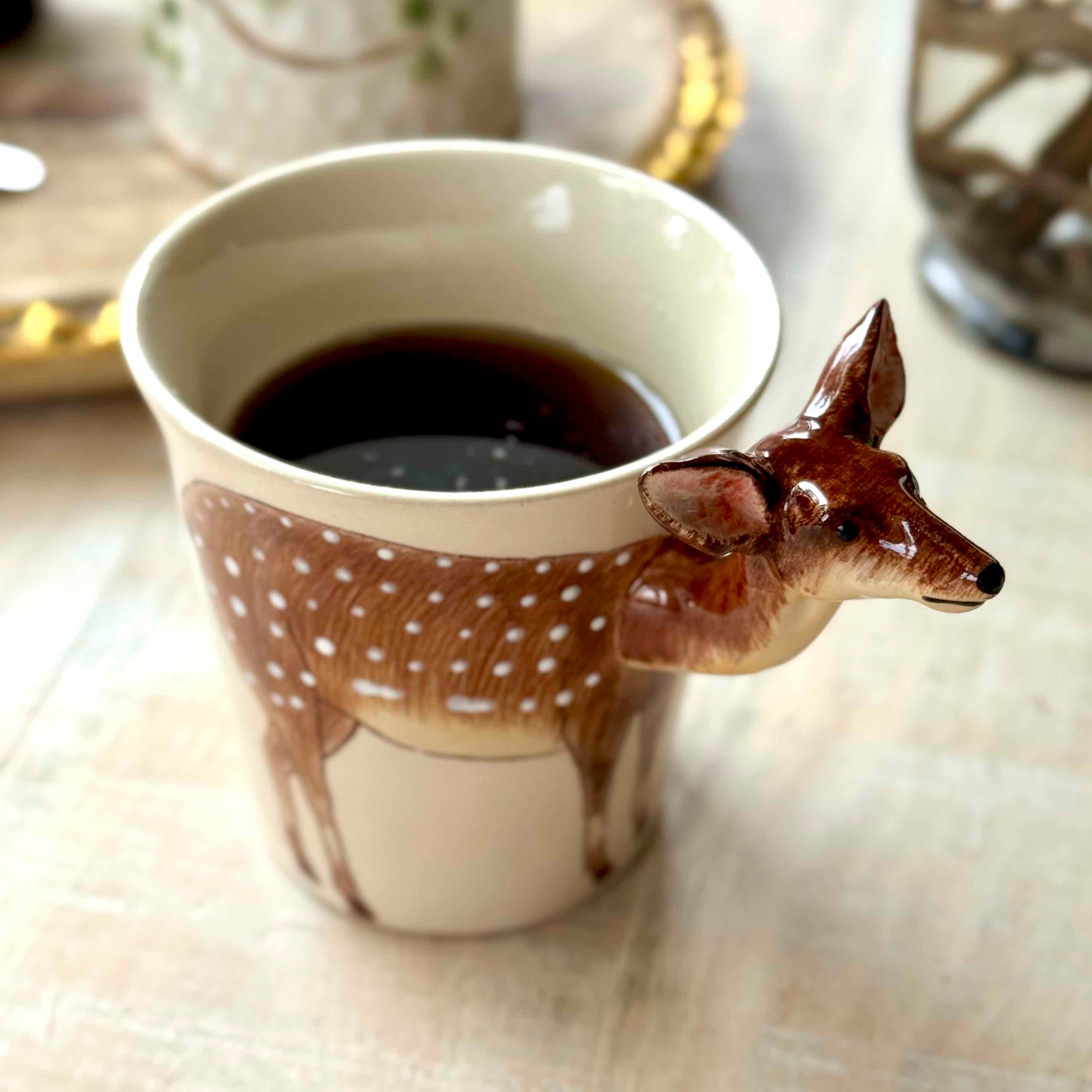 Ceramic mug with deer design filled with coffee on a light surface.