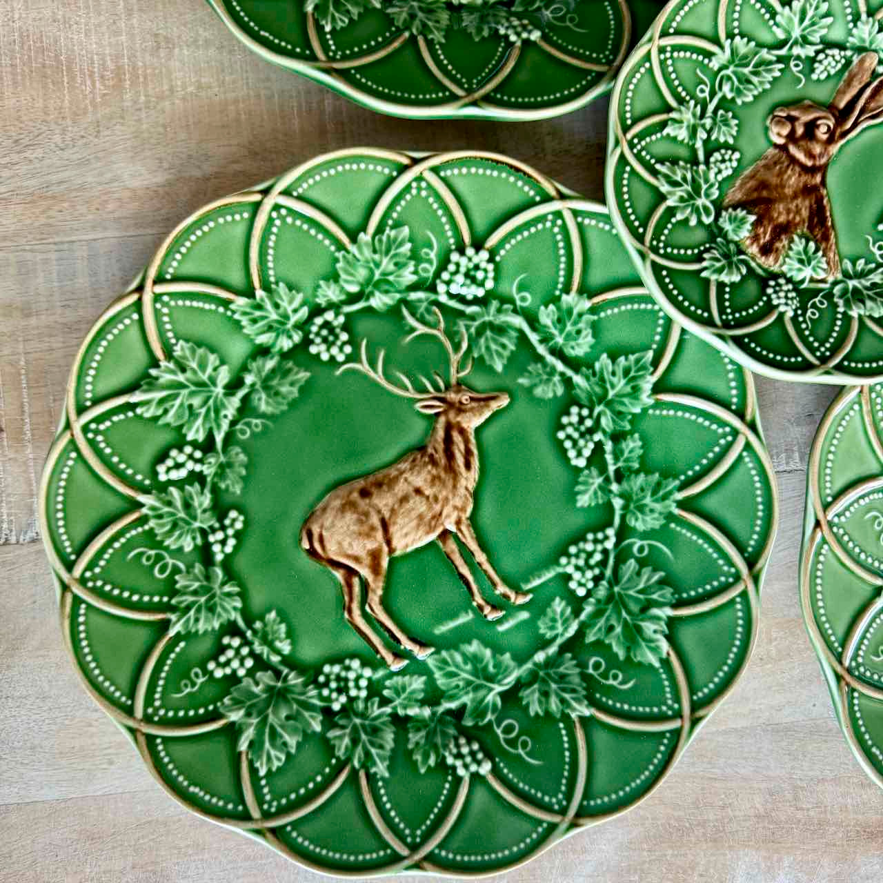 Decorative green plates with deer and floral designs on a wooden surface