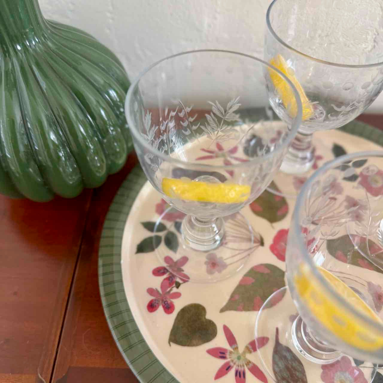 Clear glasses with lemon slices on a floral plate with a green decorative item.
