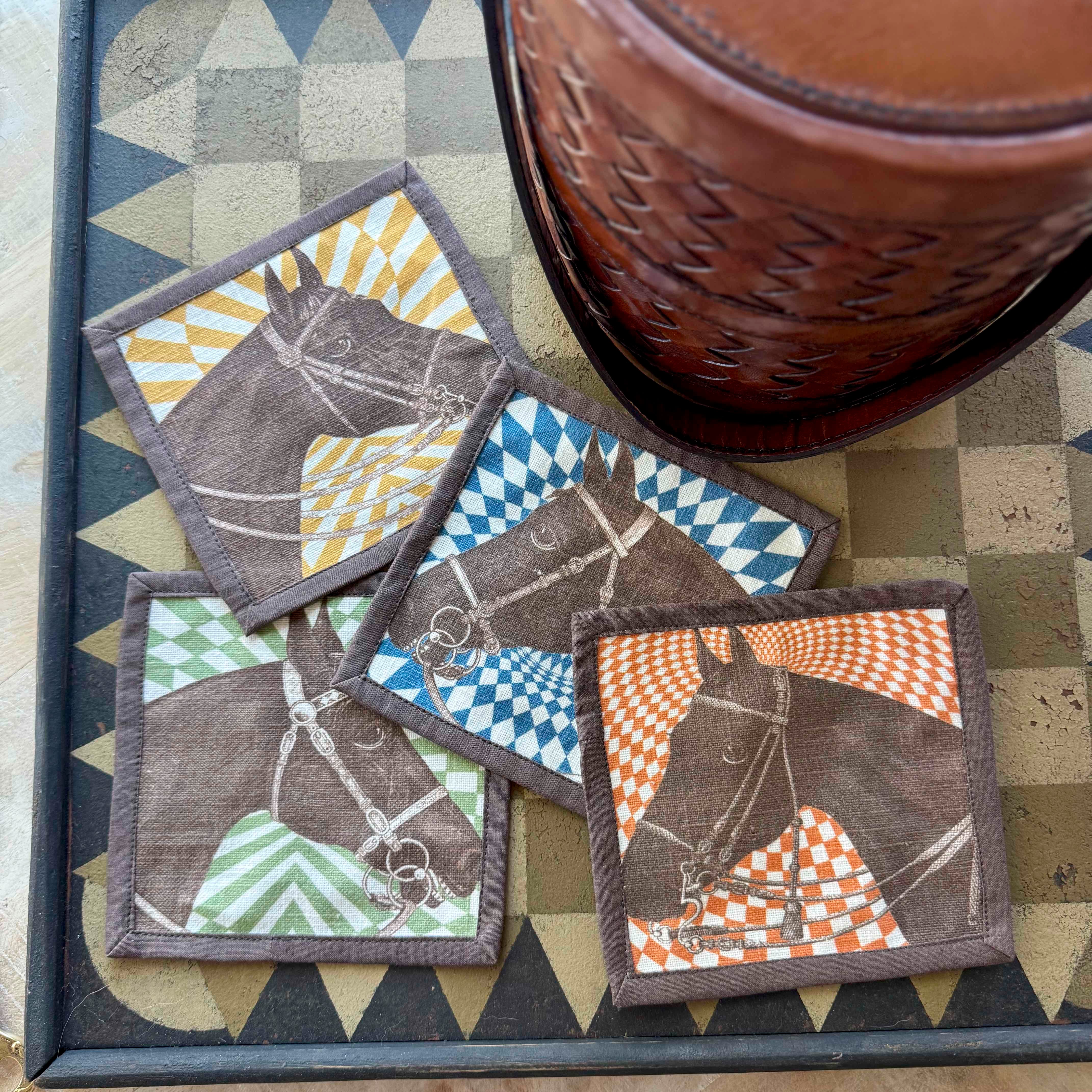 Set of four horse-themed coasters with geometric patterns on a checkered surface.