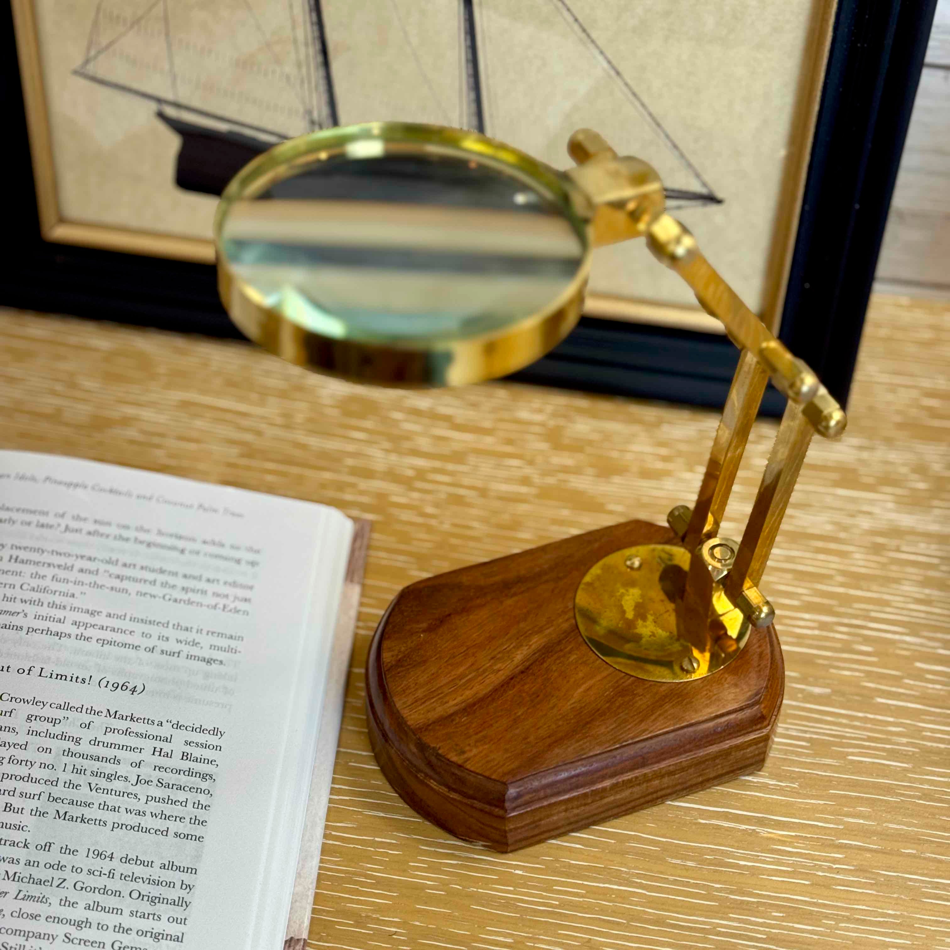 Gold magnifying glass on a wooden stand next to an open book