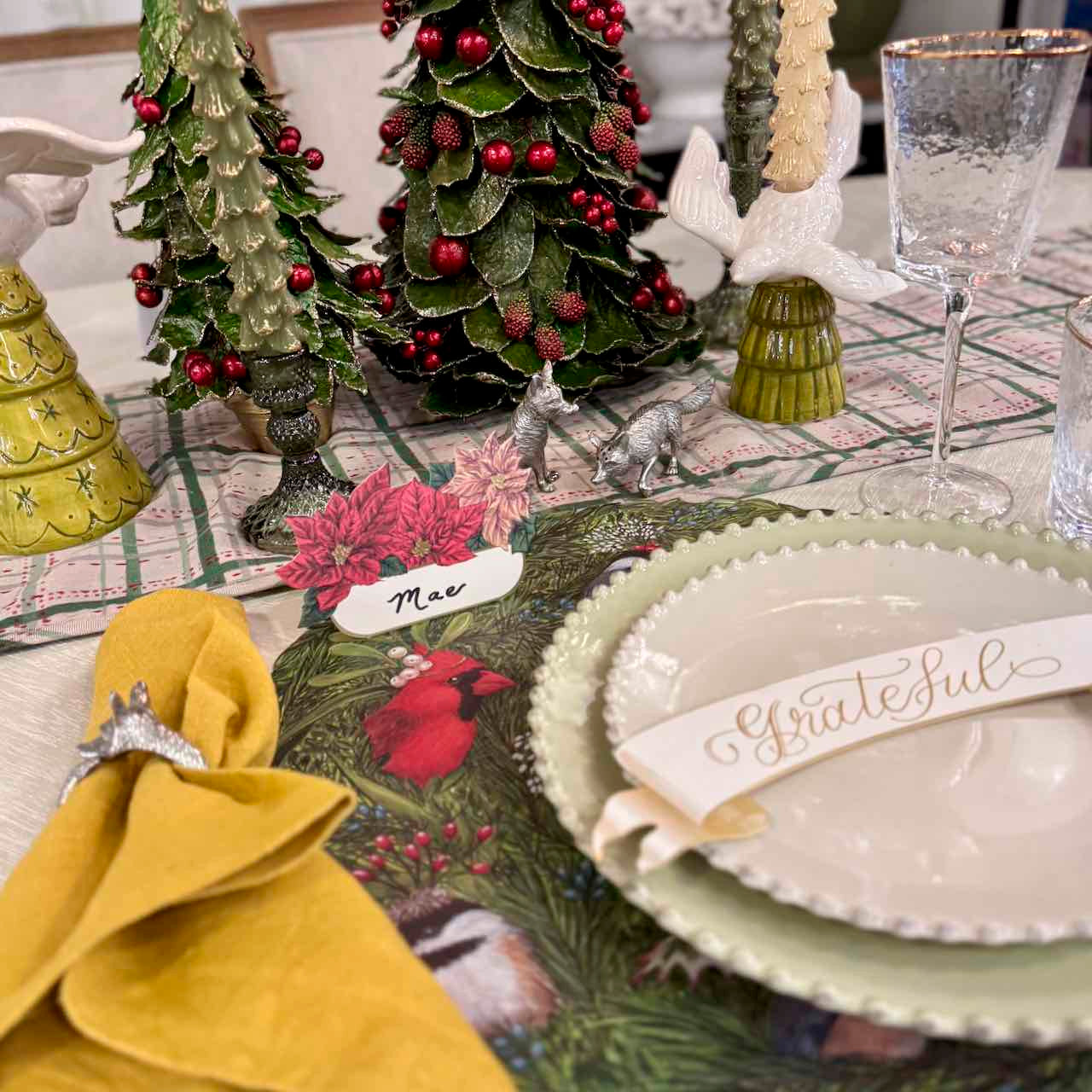 Decorative Christmas table setting with trees, place cards, and a glass.