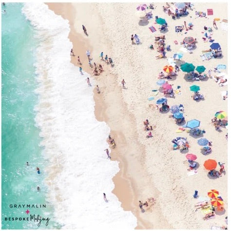 Aerial beach scene with turquoise ocean waves on the left, pale sand on the right, and many colorful beach umbrellas and small groups of people sunbathing and walking. Text in the lower left reads 'GRAYMALIN' and 'BESPOKE Mbajj'.