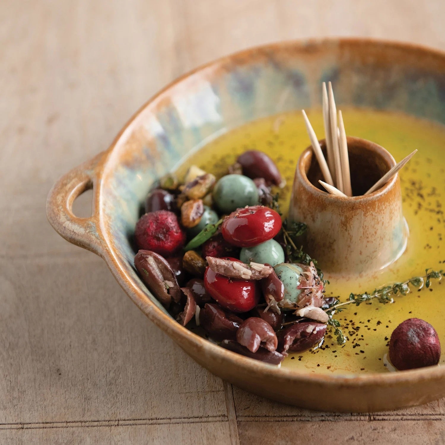 Ceramic bowl with olives, bread, and a small container of toothpicks on a wooden surface.
