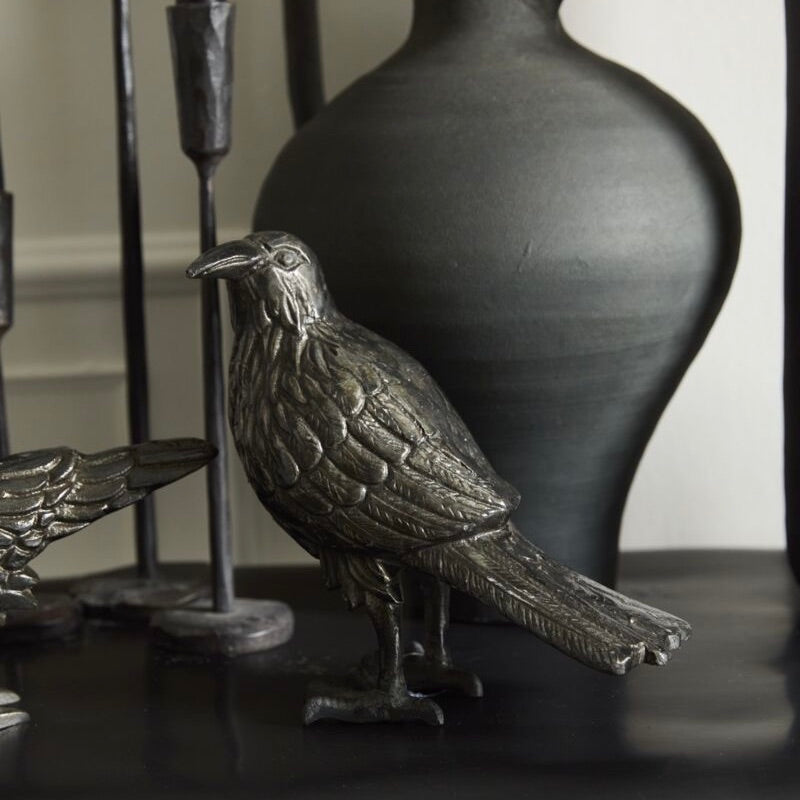 Bronze bird sculpture on a dark surface with a vase in the background
