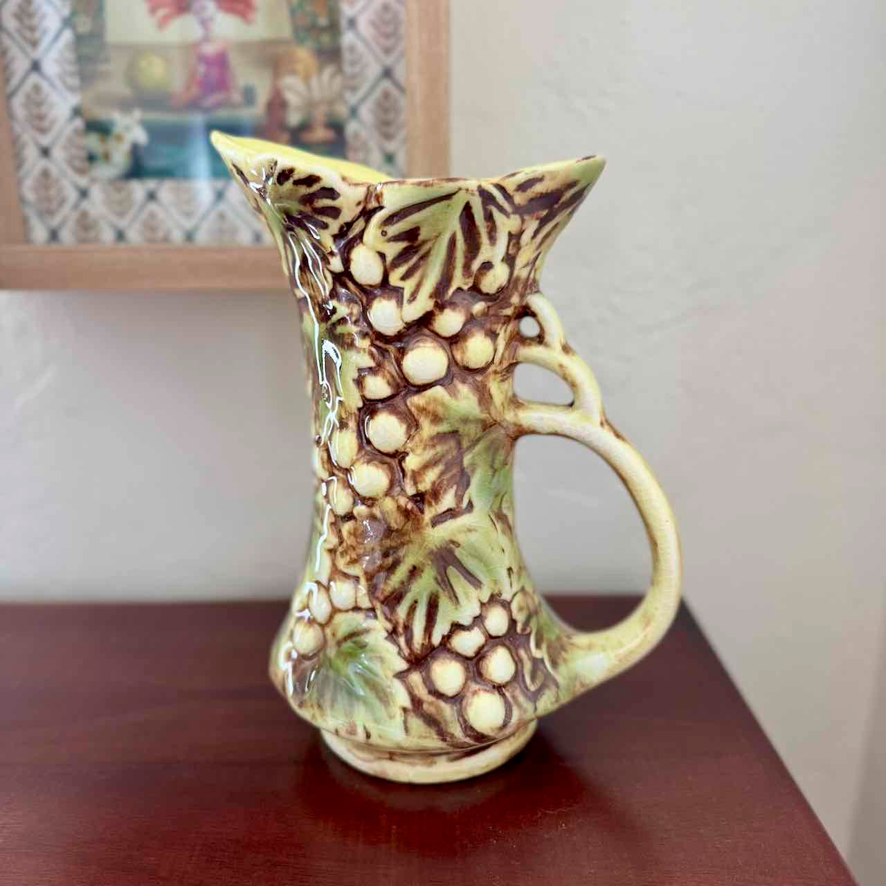 Decorative ceramic pitcher with leaf patterns on a wooden surface.