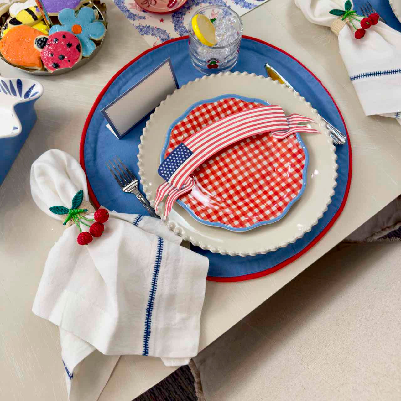 Dinner table setting with a red and white checkered plate, blue charger, and white napkin with red berries.