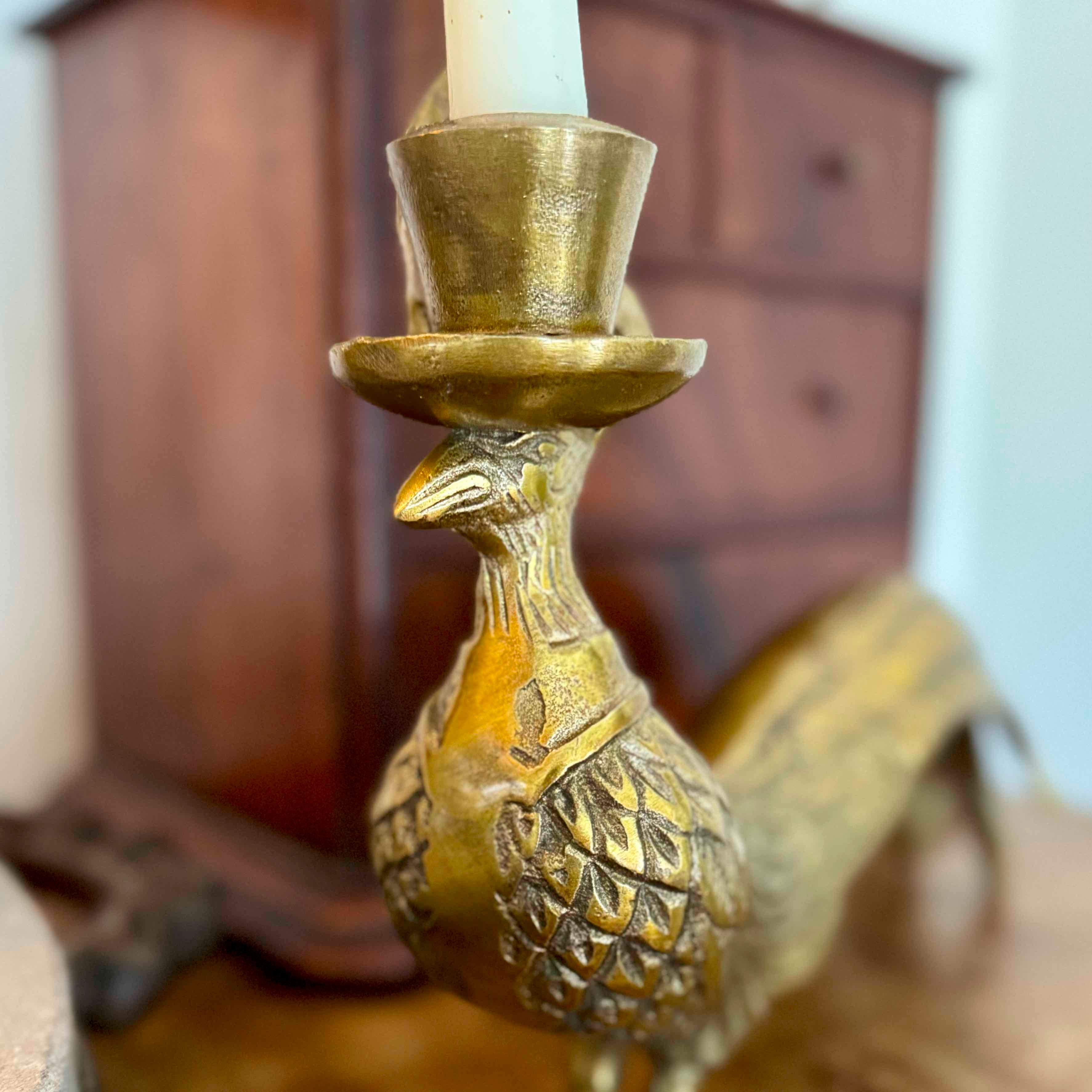 Brass peacock-shaped candle holder with a candle inside, set against a blurred wooden cabinet background.