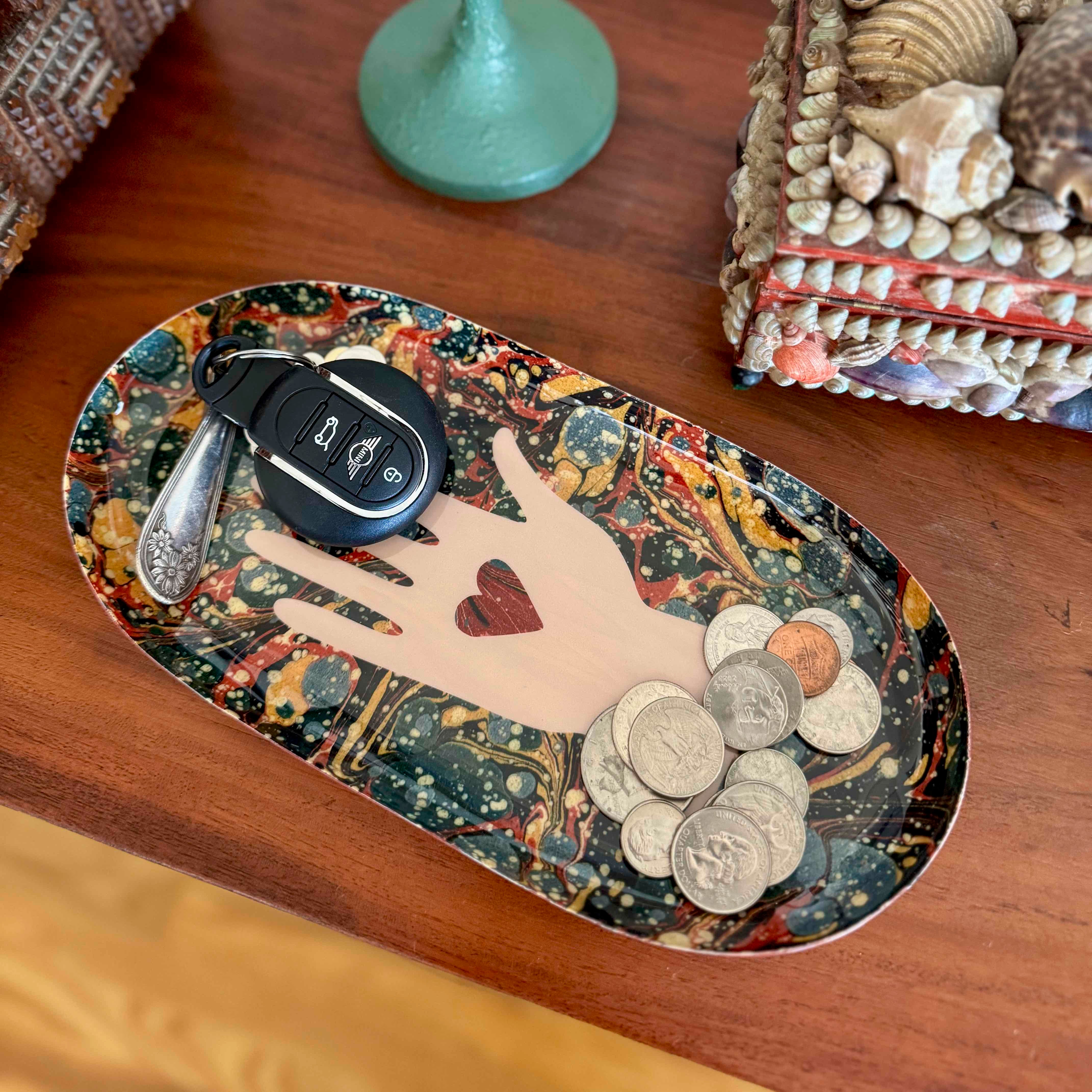 Decorative tray with a hand holding a heart design, coins, and keys on a wooden surface.