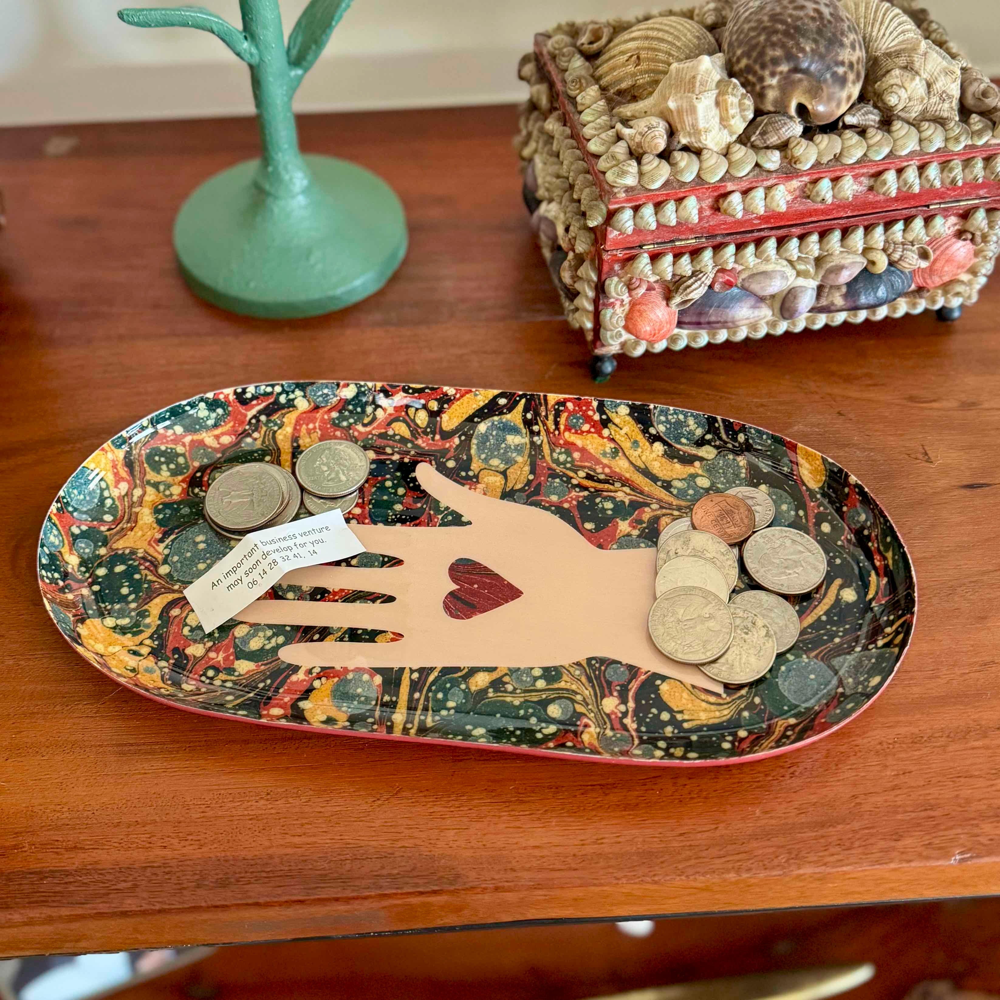 Decorative tray with hand design and coins on a wooden surface
