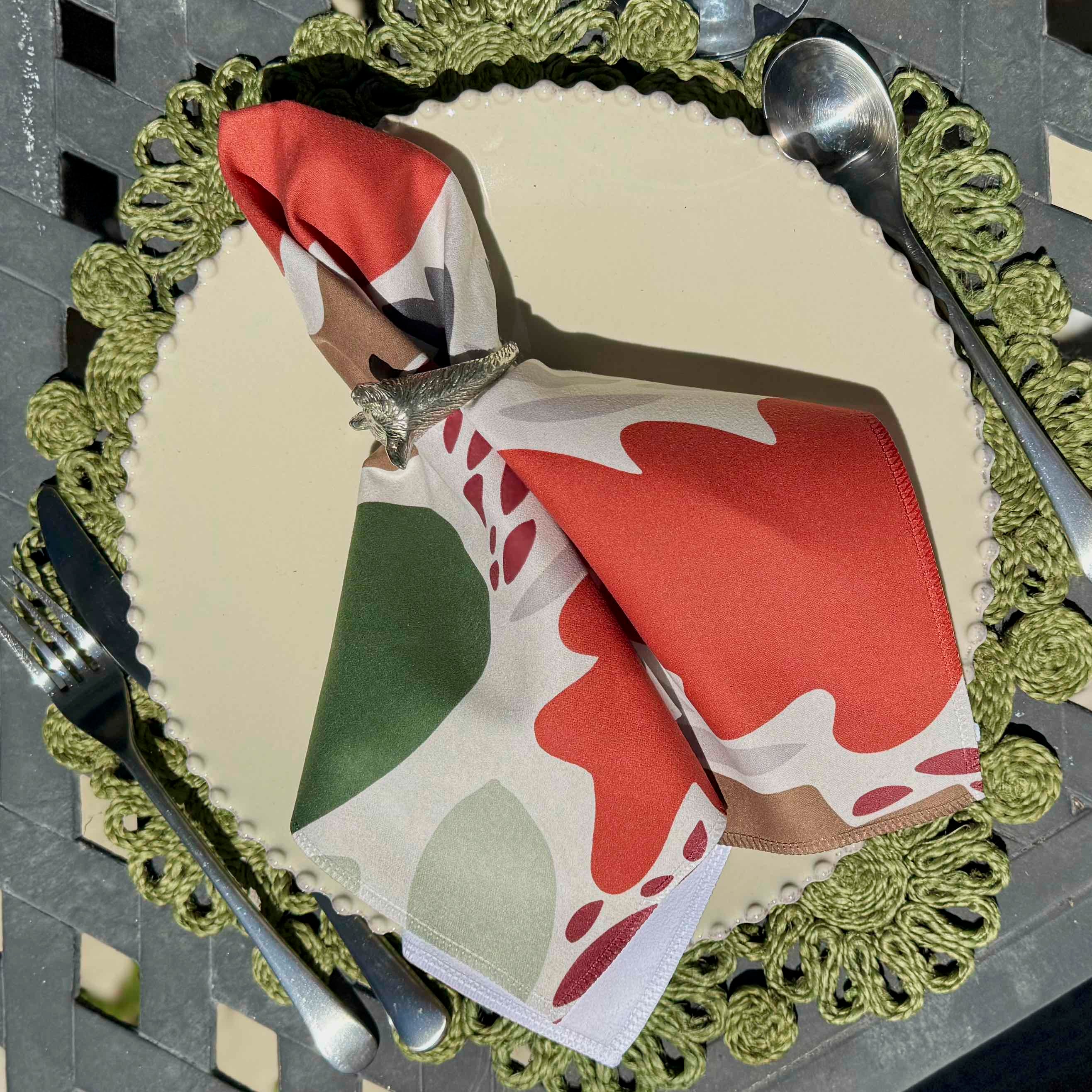 Decorative table setting with a folded napkin on a plate, surrounded by cutlery and a green doily.